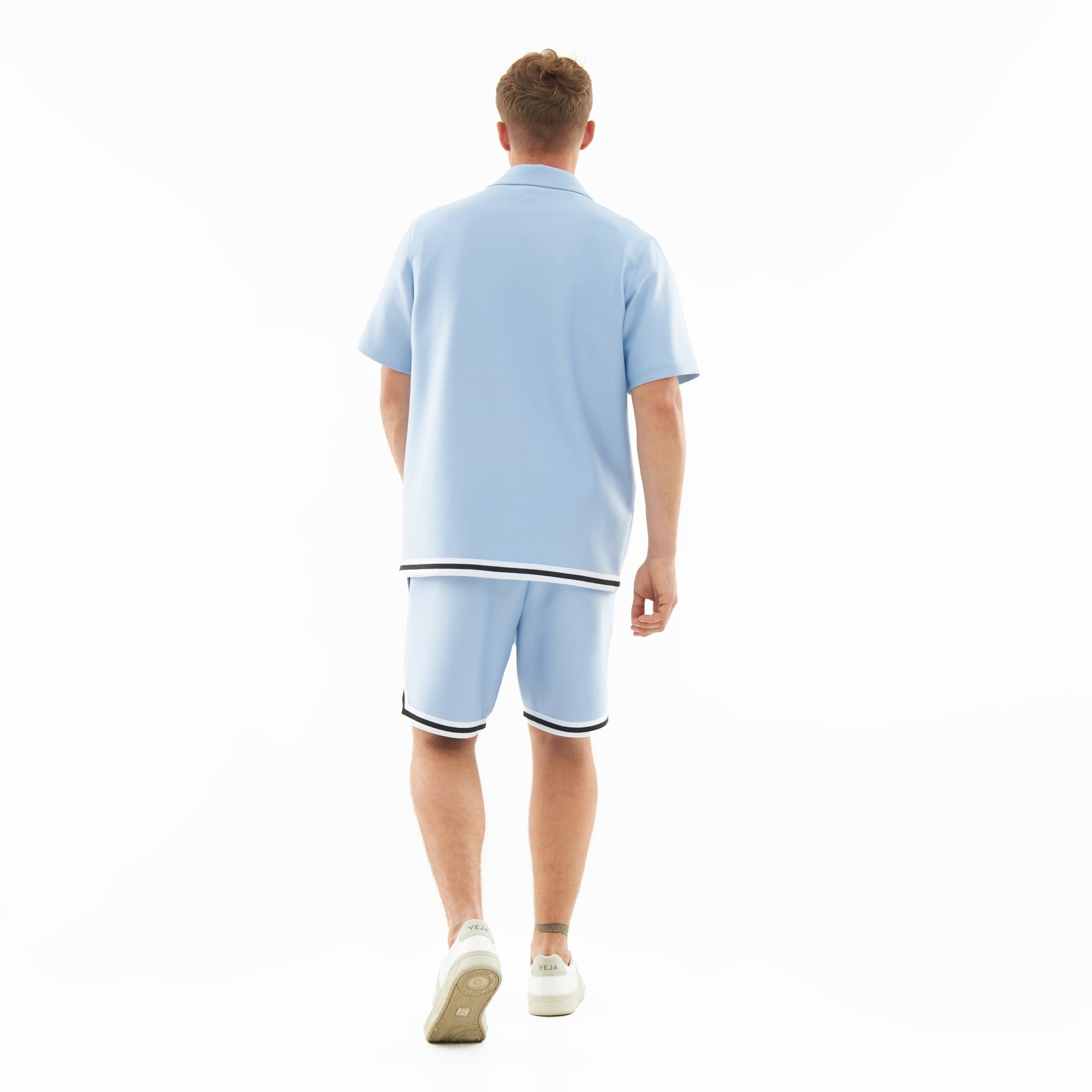 Mann von hinten trägt hellblaues, locker geschnittenes Hemd und Shorts mit schwarzen und weißen Saumstreifen