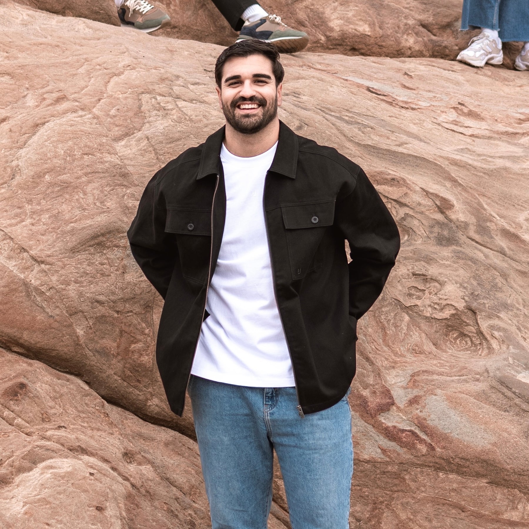 Mann trägt Overshirt 'Cameron' in Schwarz, kombiniert mit weißem T-Shirt und blauen Jeans, vor Felsen