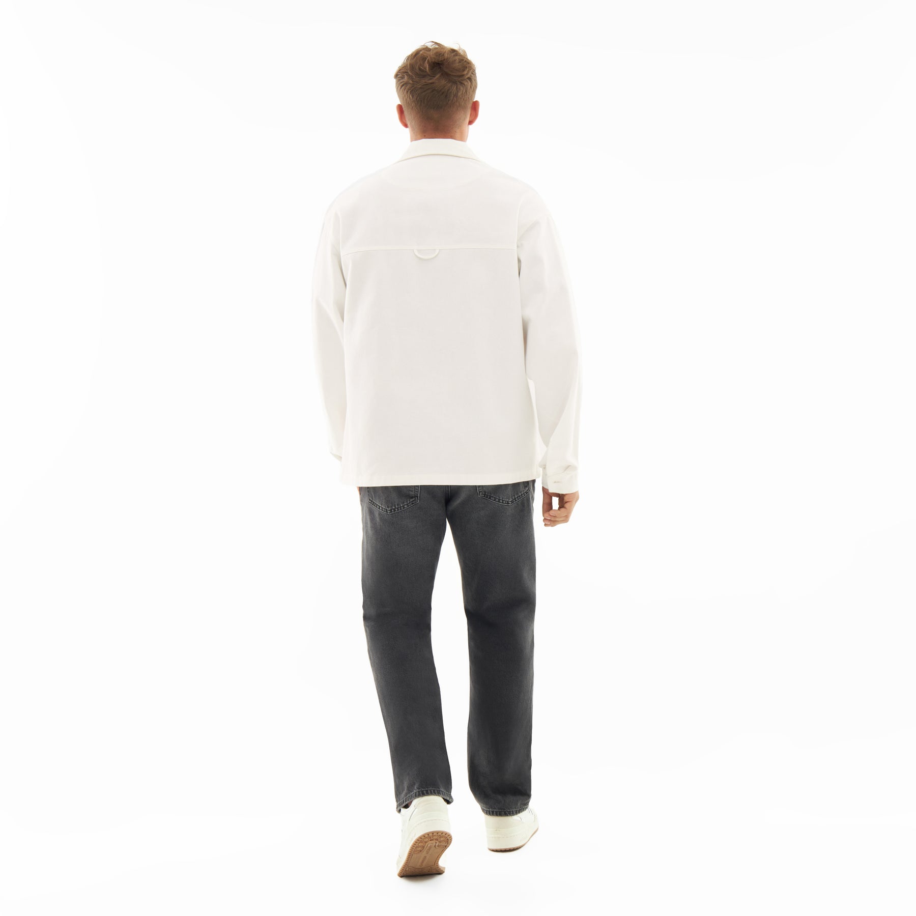 Rückansicht eines Mannes mit weißem Overshirt 'Cameron', dunkler Jeans und weißen Schuhen