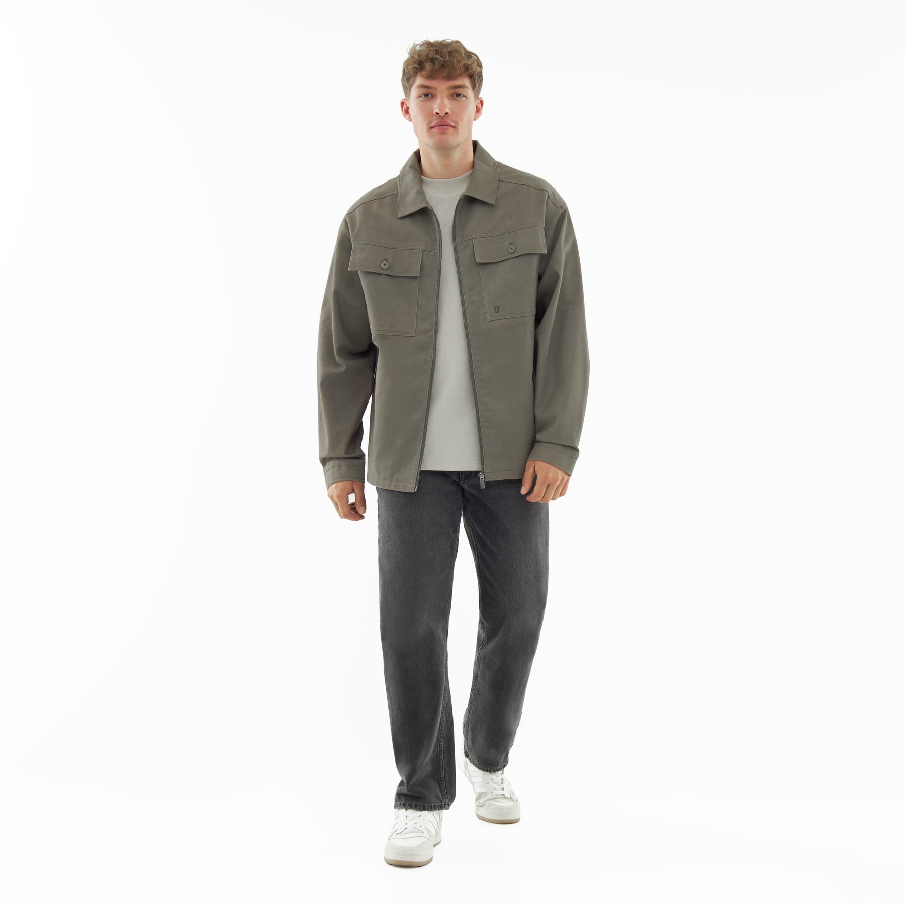 Mann trägt olivgrüne Overshirt 'Cameron' aus Baumwolle mit zwei Brusttaschen, kombiniert mit weißem T-Shirt, schwarzen Jeans und weißen Sneakern