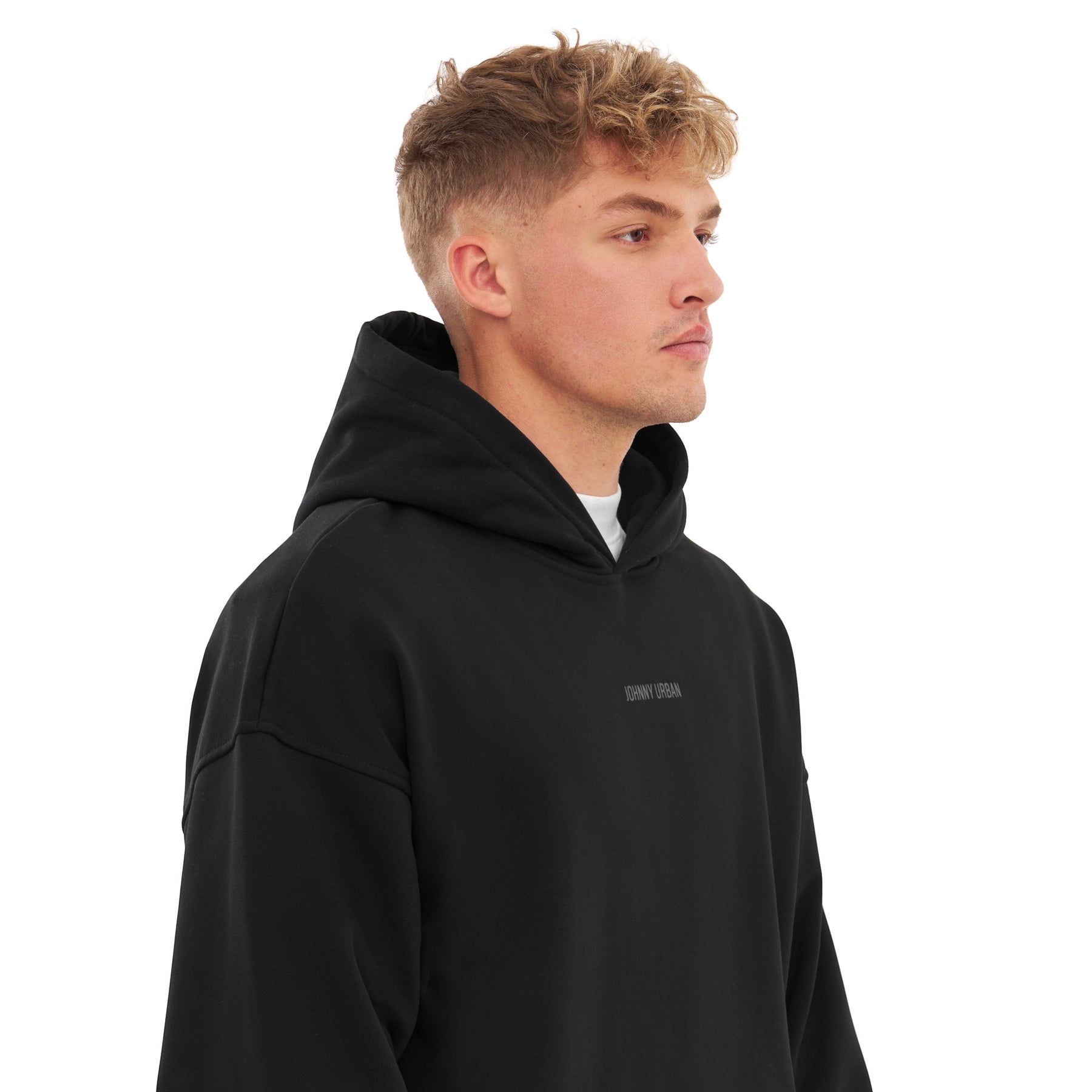 Junger Mann trägt schwarzen oversized Hoodie 'Cody' mit Kapuze und 'Johnny Urban' Print vorne