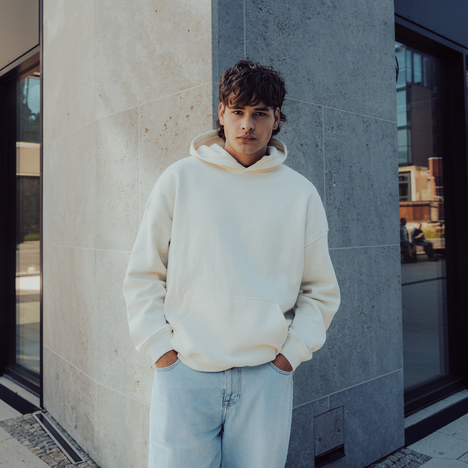 Mann trägt oversized Hoodie 'Cody' von Johnny Urban in weiß vor modernem Gebäude