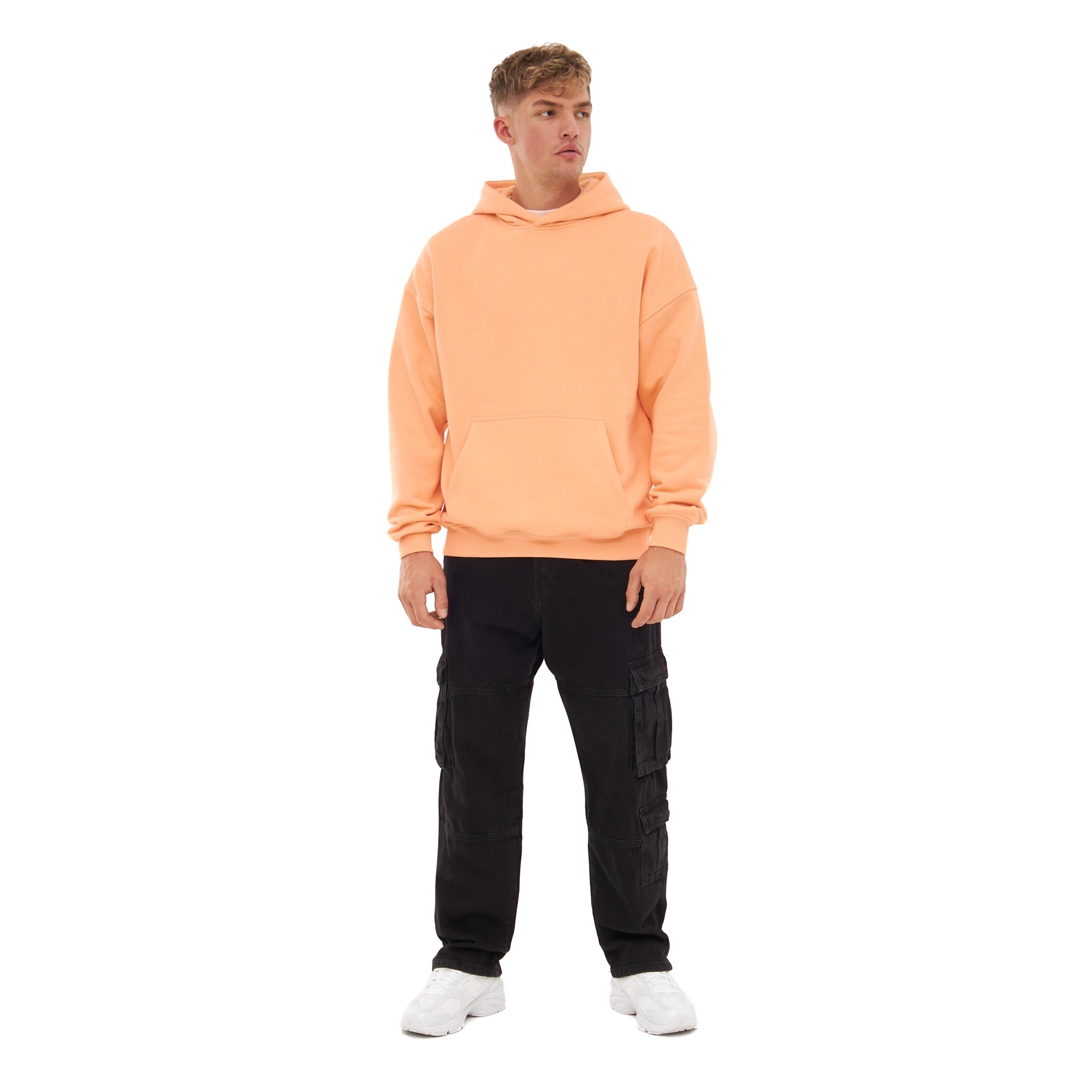 Mann mit oversized Hoodie 'Cody' in Pfirsich, schwarzen Cargo-Hosen und weißen Sneakers