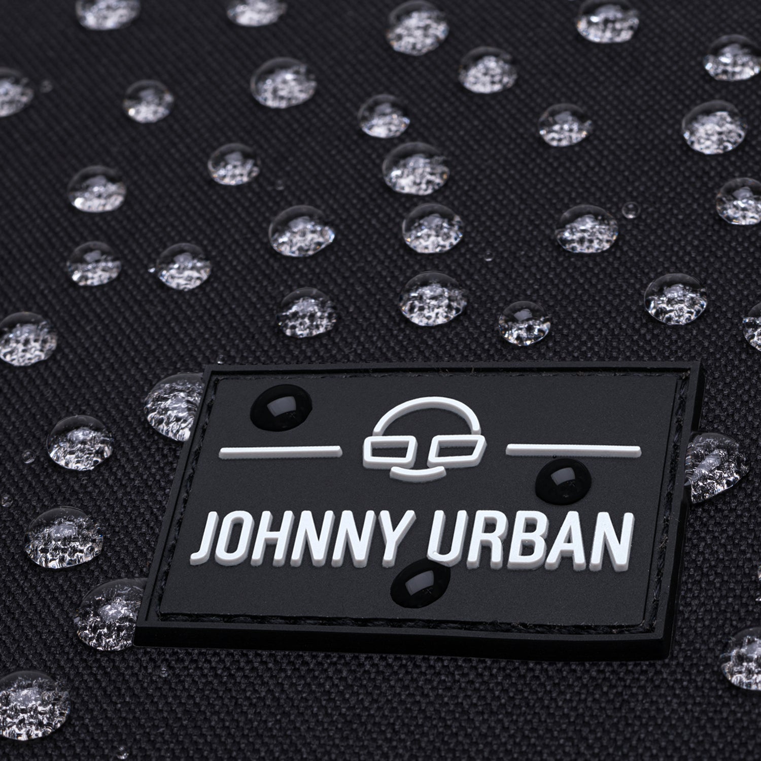 Nahaufnahme des Johnny Urban Logos auf einem wasserabweisenden Rolltop-Rucksack 'Allen Large' mit Wassertröpfchen