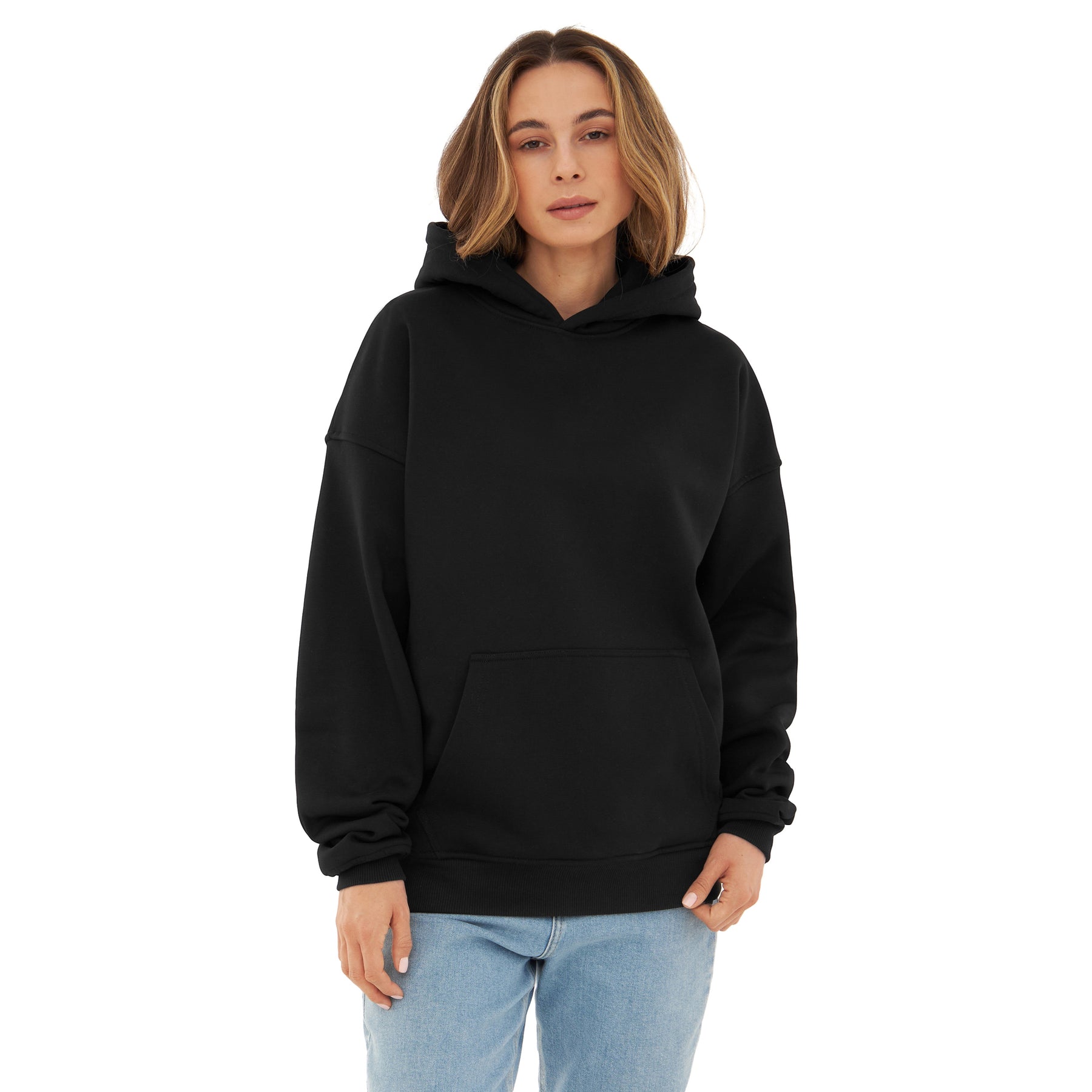 Frau trägt oversized Hoodie 'Cody' in Schwarz mit Kapuze und Kängurutasche, kombiniert mit blauen Jeans