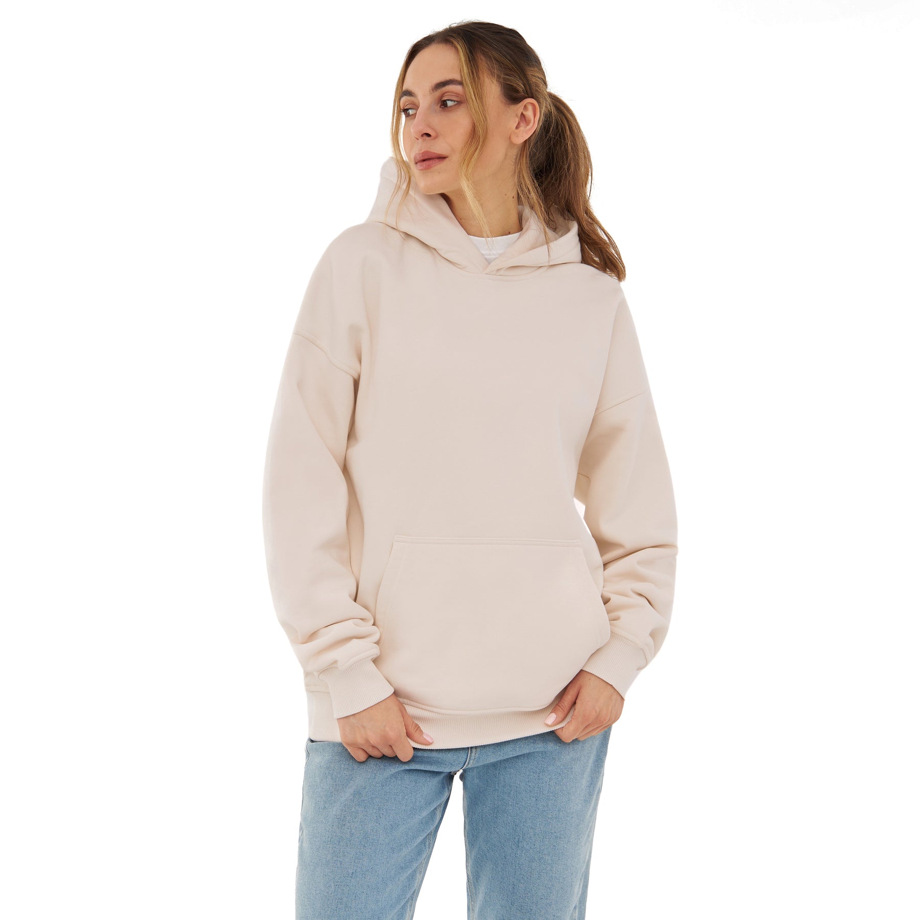 Frau trägt oversized Hoodie 'Cody' in Beige mit Kapuze und Kängurutasche, kombiniert mit blauen Jeans