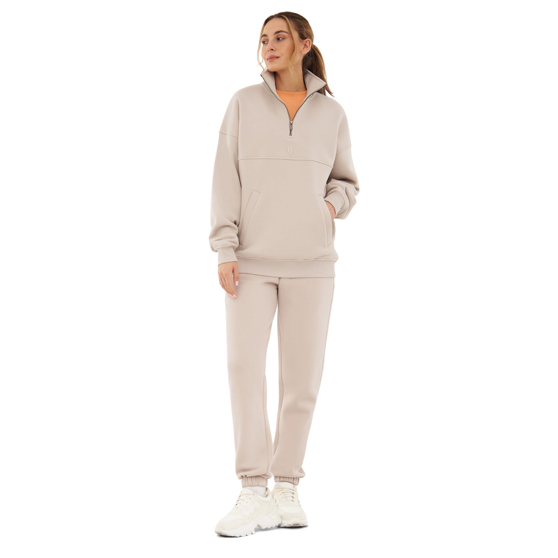Frau trägt sandfarbene Jogginghose 'Owen' mit lockerem, halblangem Pullover und weißen Sneakern