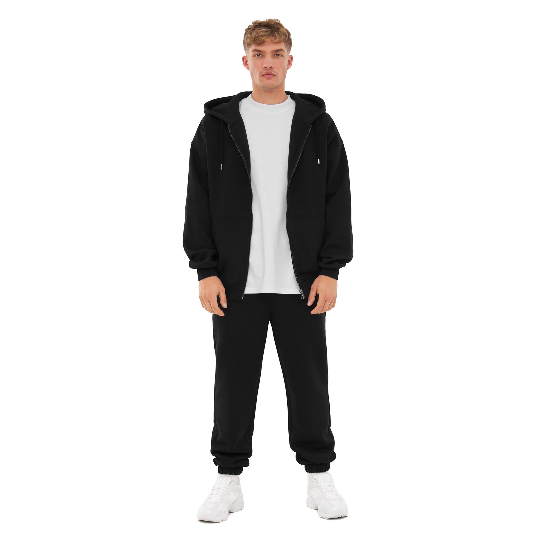 Mann trägt schwarze Jogginghose 'Owen' von Johnny Urban mit weißem T-Shirt, schwarzer Zip-Hoodie und weißen Sneakern