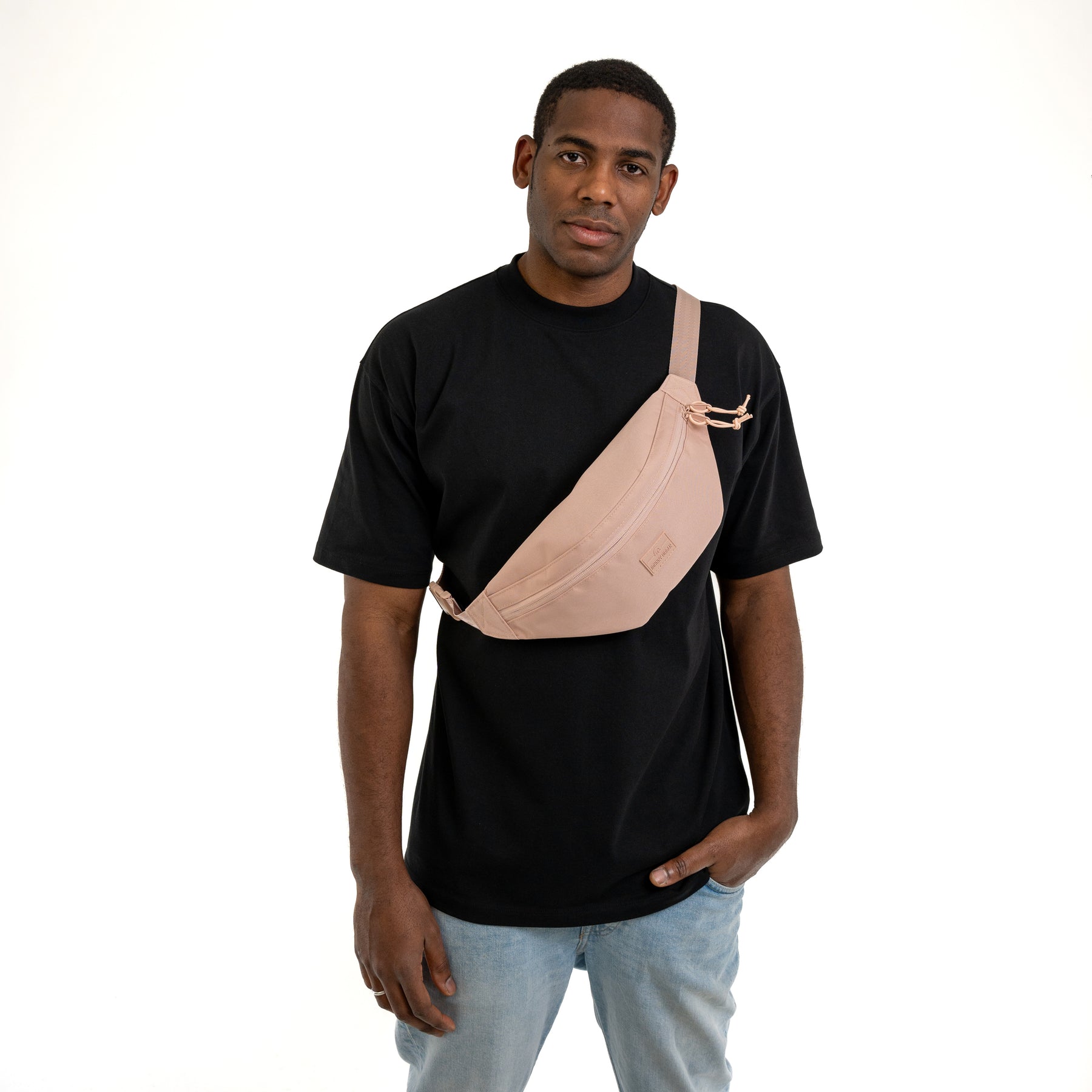 Mann trägt Bauchtasche 'Erik Large' in Rosa quer über der Brust, kombiniert mit schwarzem T-Shirt und blauer Jeans
