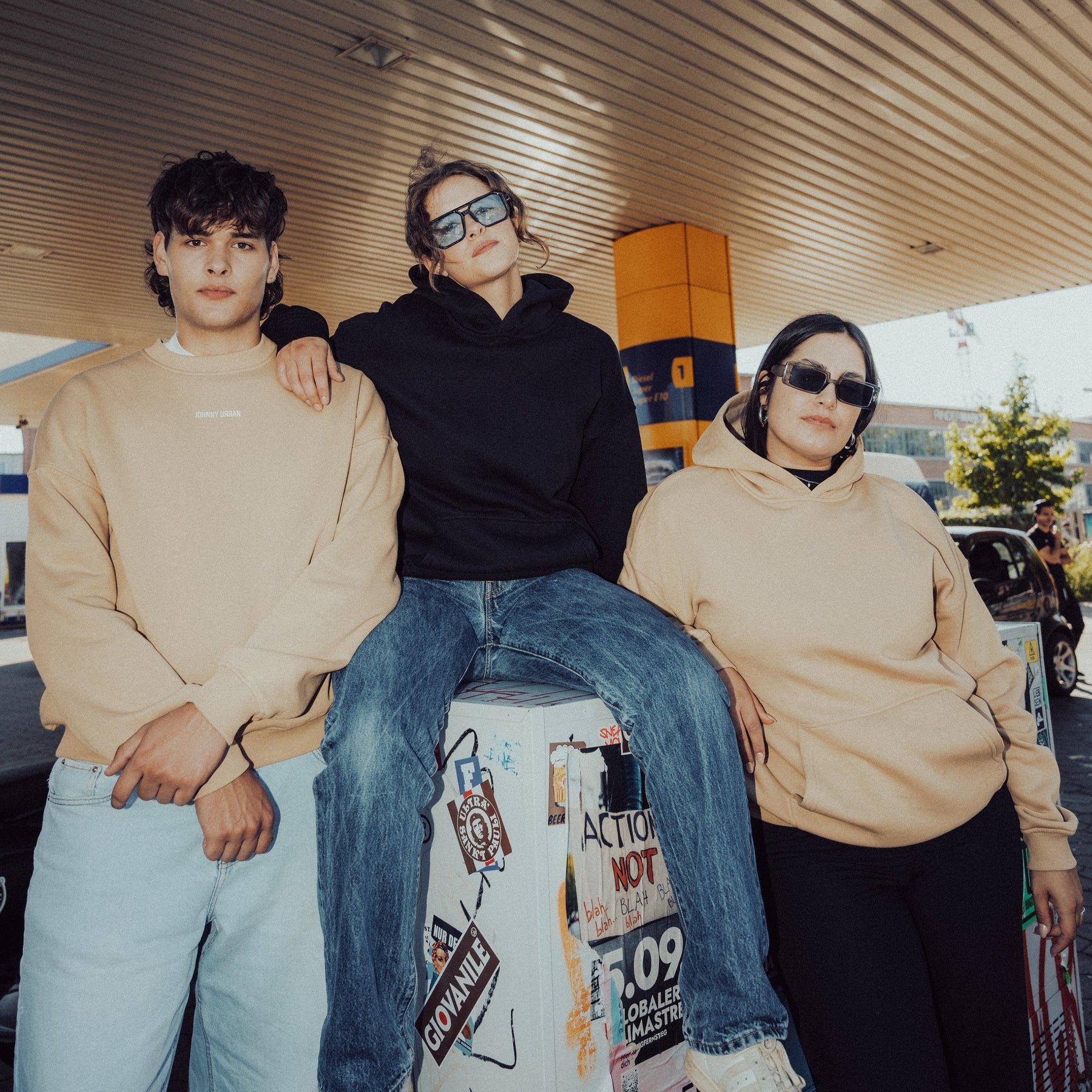 Drei junge Menschen tragen oversized Hoodies 'Cody', zwei in Beige und einer in Schwarz, in urbaner Umgebung