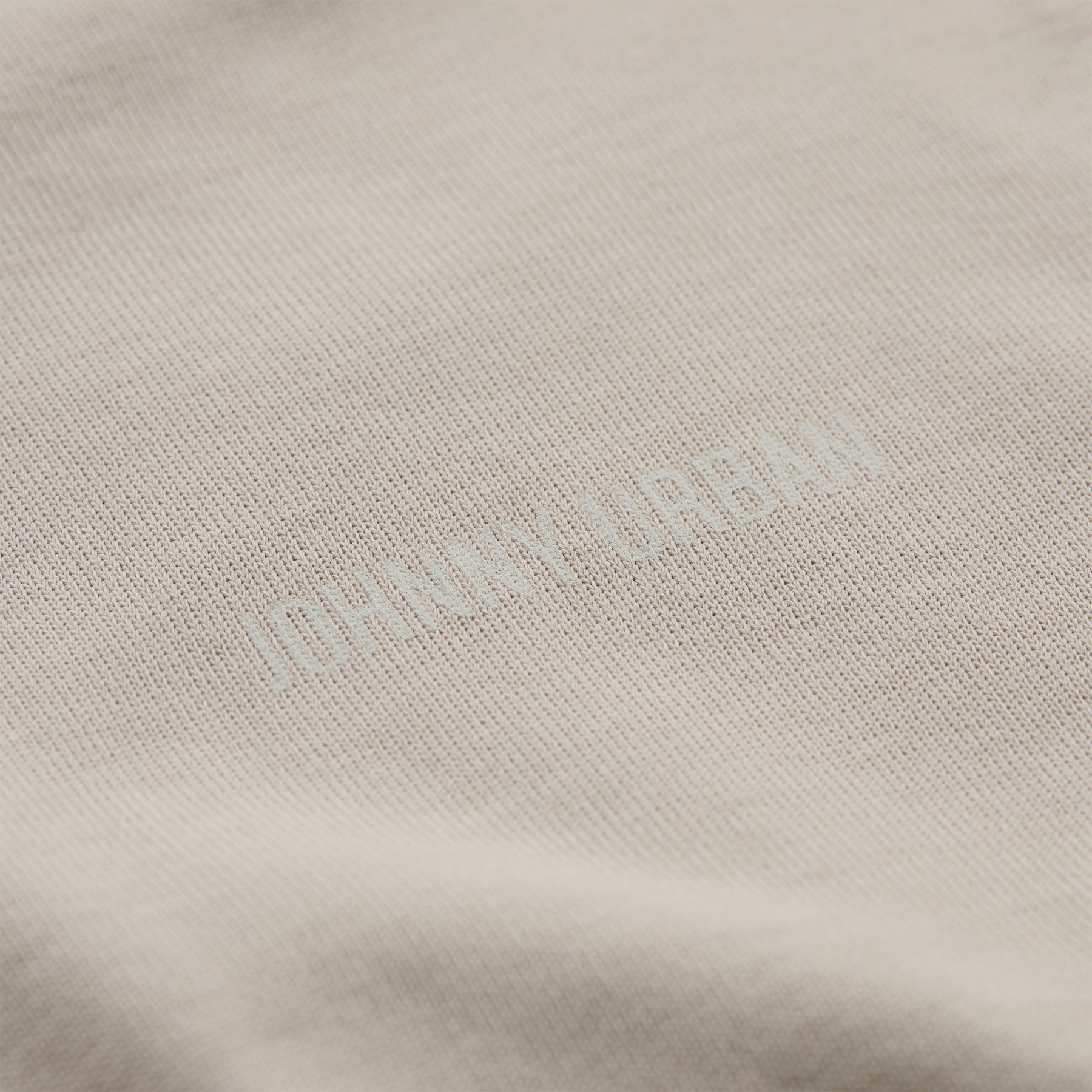 Detailaufnahme eines beigen T-Shirts mit geprägtem 'Johnny Urban' Schriftzug
