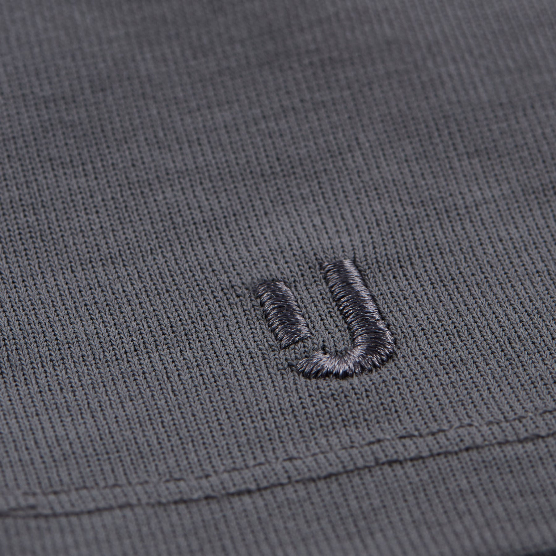 Nahaufnahme des grauen Baumwollstoffs eines T-Shirts mit eingesticktem 'ju'-Logo