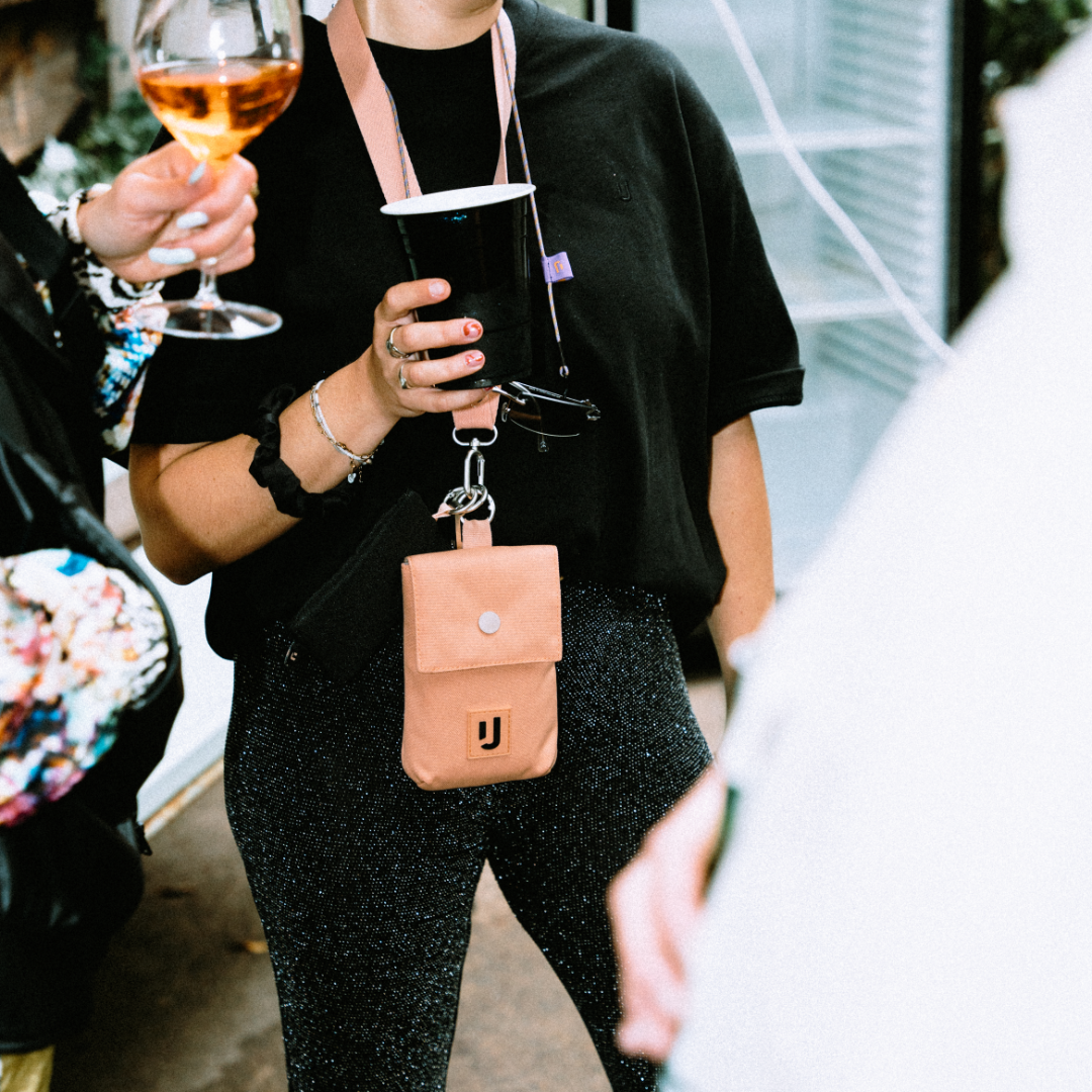 Person trägt die peachfarbene Neck Pouch 'Juno' von Johnny Urban mit Schlüsselbund und Becher