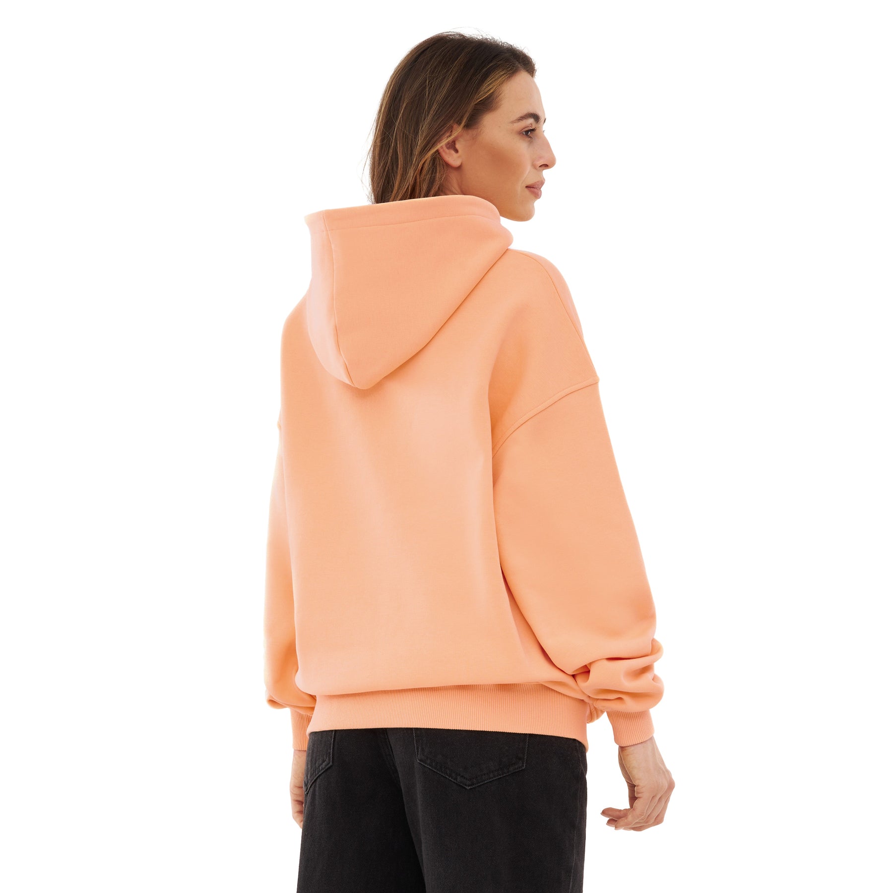 Rückansicht eines Modells mit oversized Kapuzenpullover 'Cody' in Pfirsich und schwarzer Hose