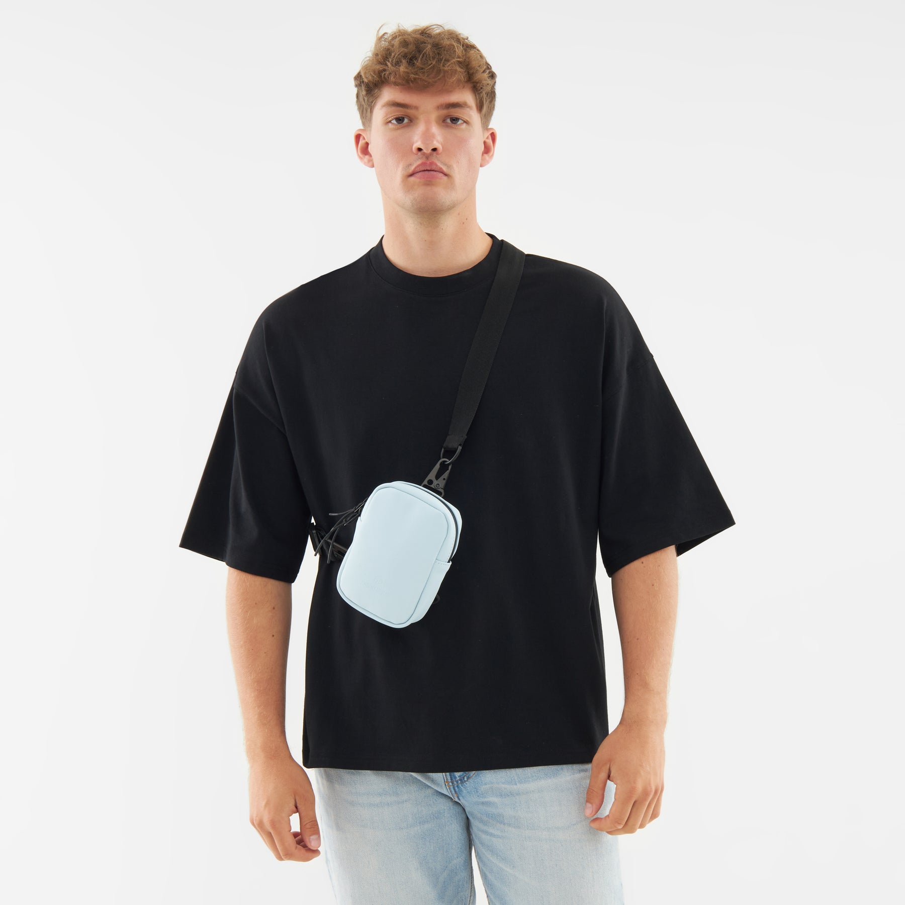 Junger Mann trägt die hellblaue Front Pack 'Toby' Crossbody-Tasche von Johnny Urban über schwarzem T-Shirt und blauer Jeans