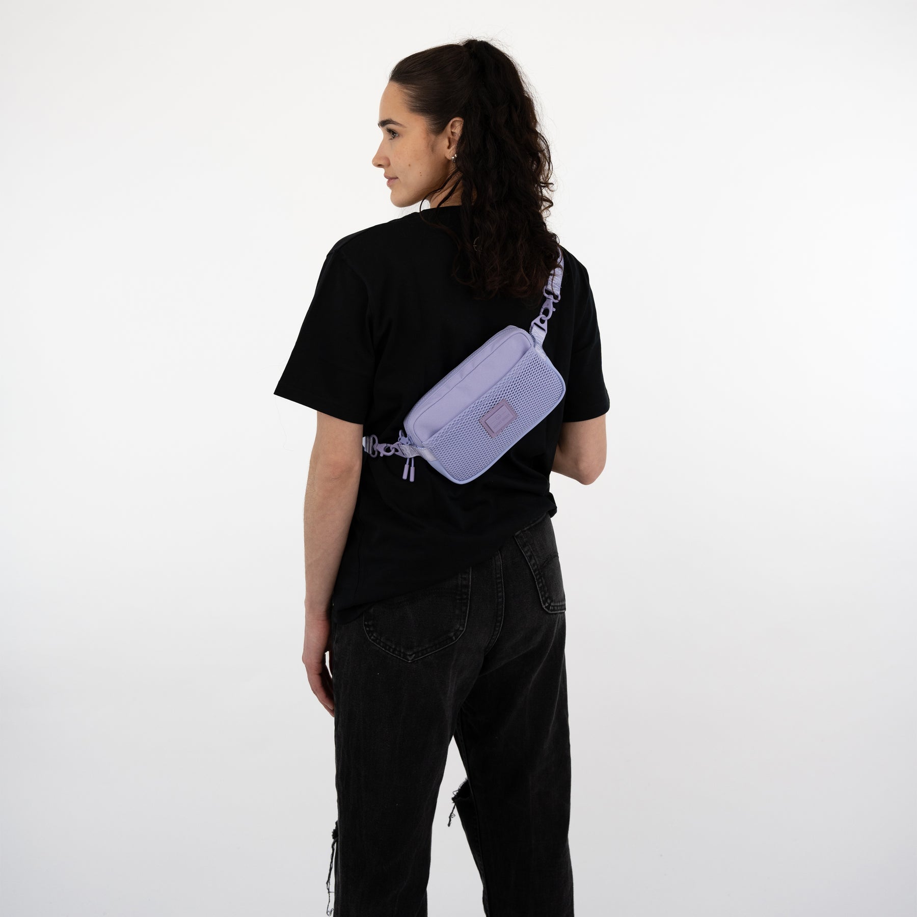 Frau mit schwarzem T-Shirt und Hose trägt lilafarbene Umhängetasche 'Elliot' quer am Rücken