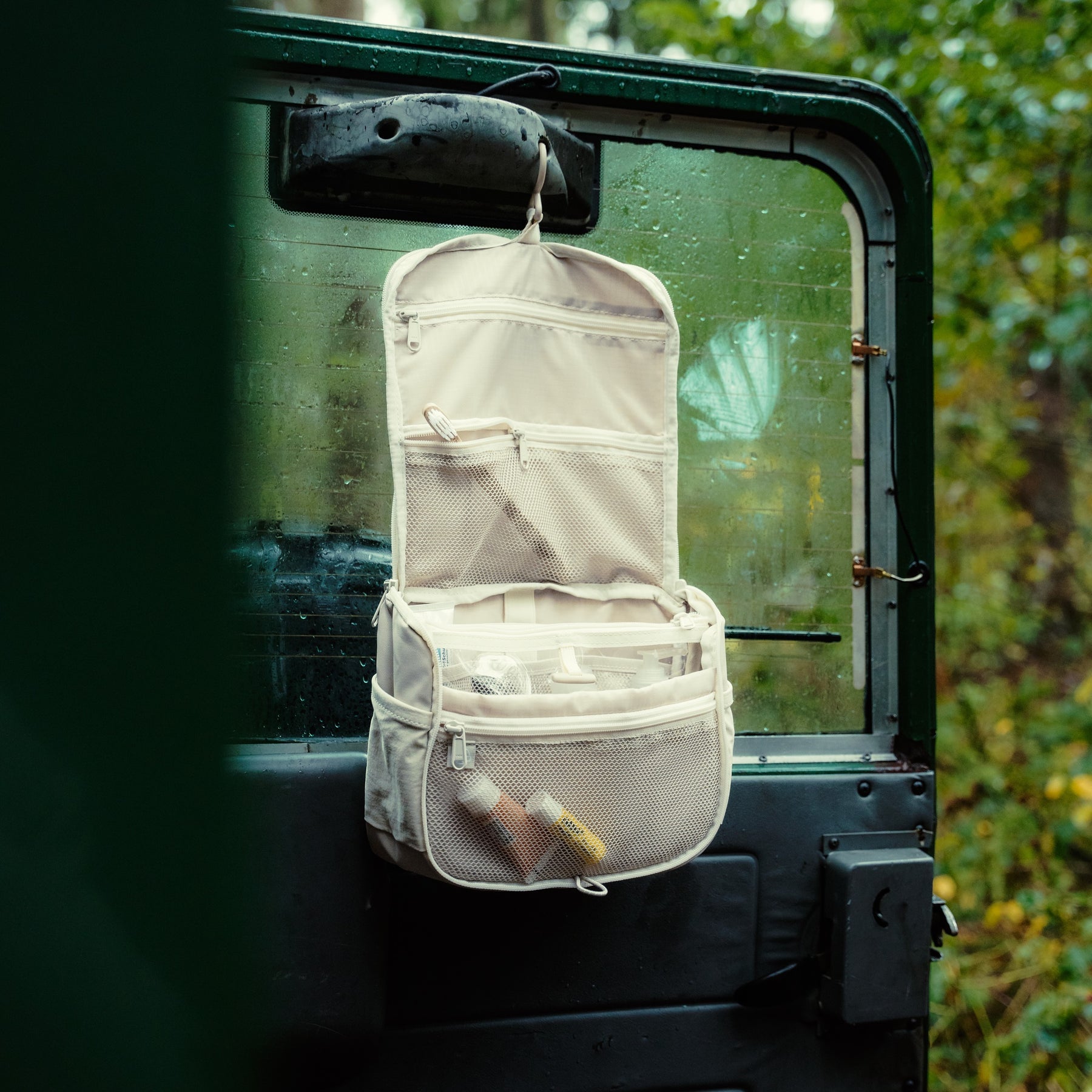 Beige Kulturtasche 'Logan' von Johnny Urban mit mehreren Taschen hängt an einer Autotür