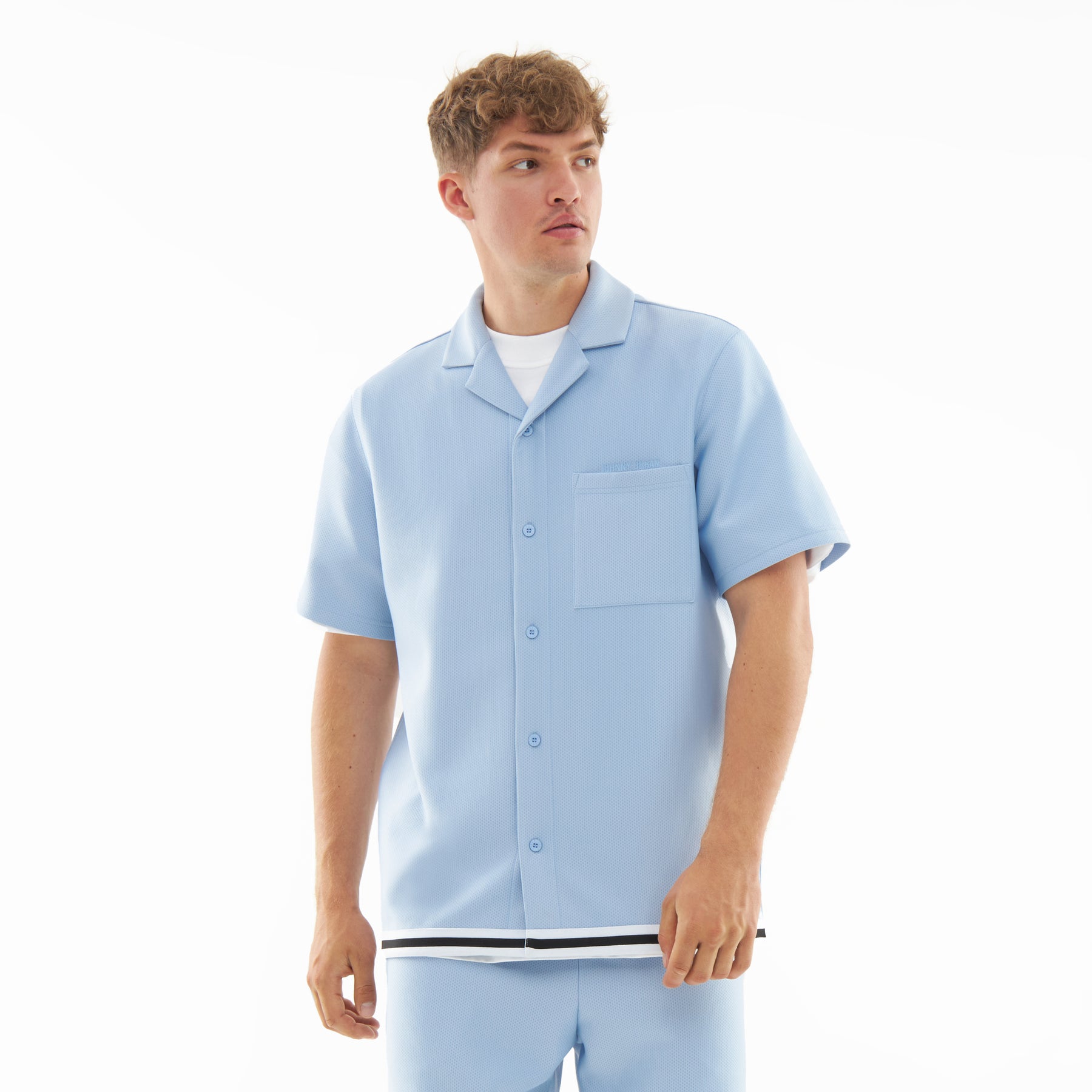 Mann trägt hellblaues, kurzärmliges Hemd aus leichtem Material mit Brusttasche und weiß-schwarzem Saumband aus dem Set 'Parker'