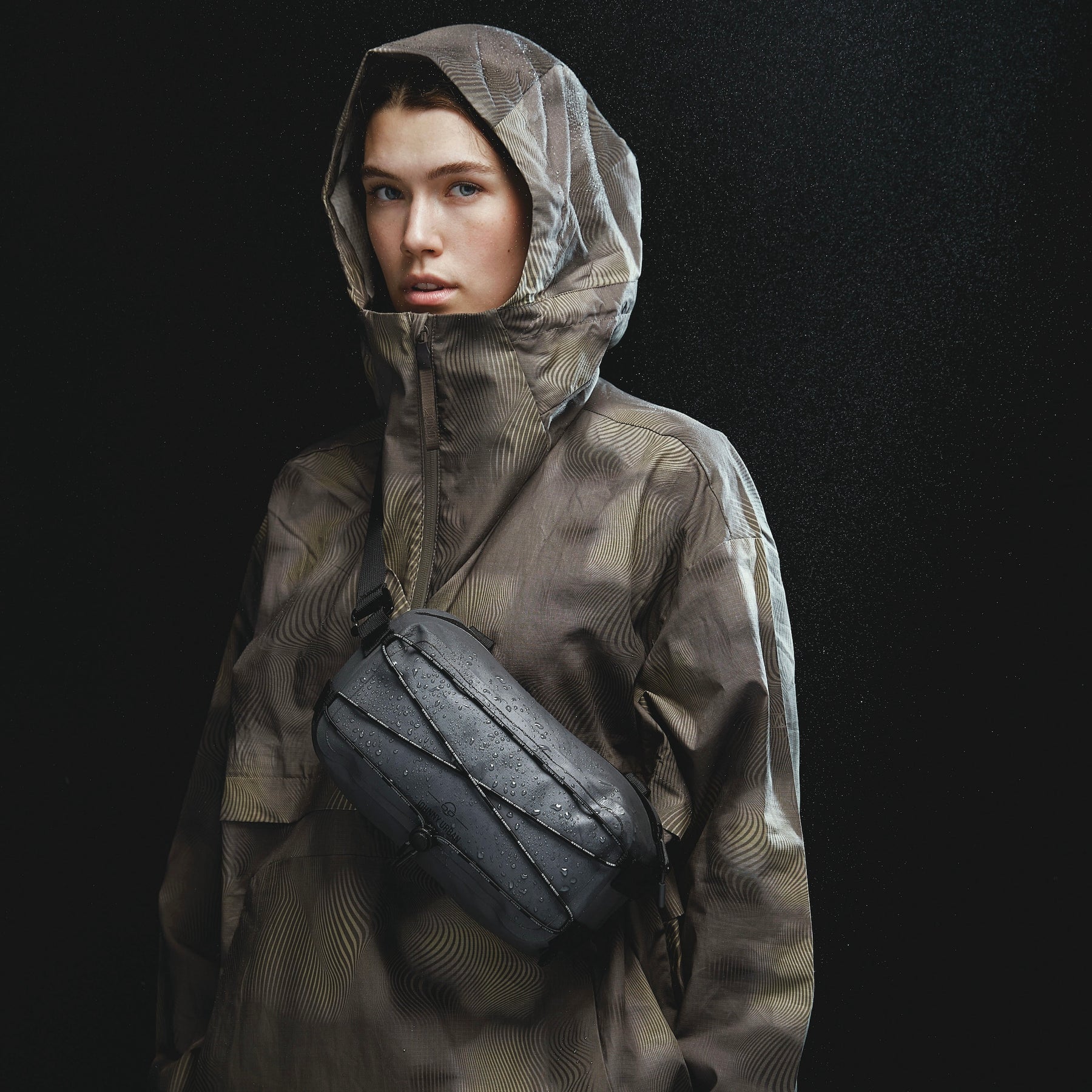 Wasserdichte Lenkertasche Fahrrad 'Arlo' in Schwarz mit Wasserperlen, getragen über die Schulter mit braunem Regenmantel