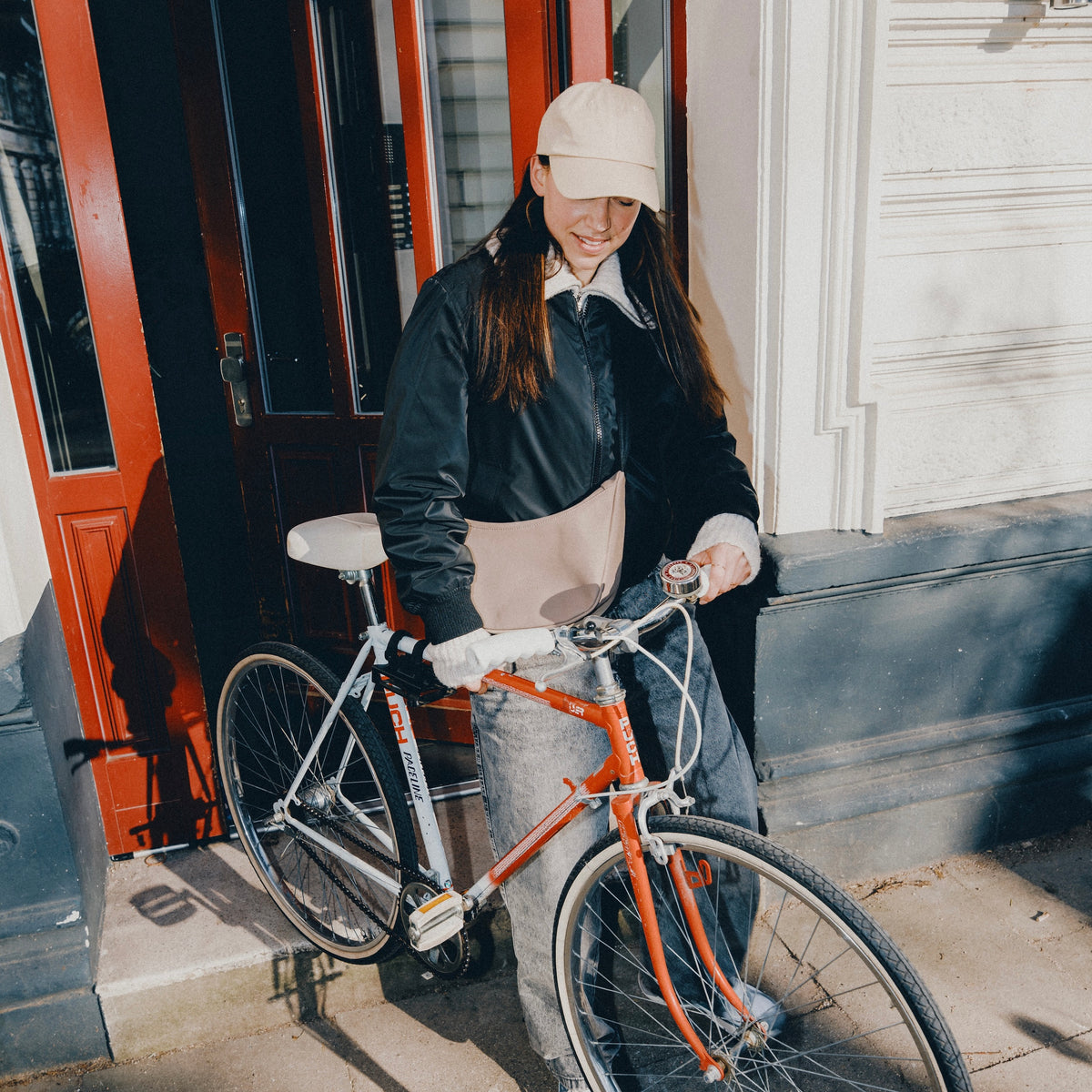 Frau mit beigefarbener Half Moon Bag 'Rory' lehnt an rotem Fahrrad vor Gebäude