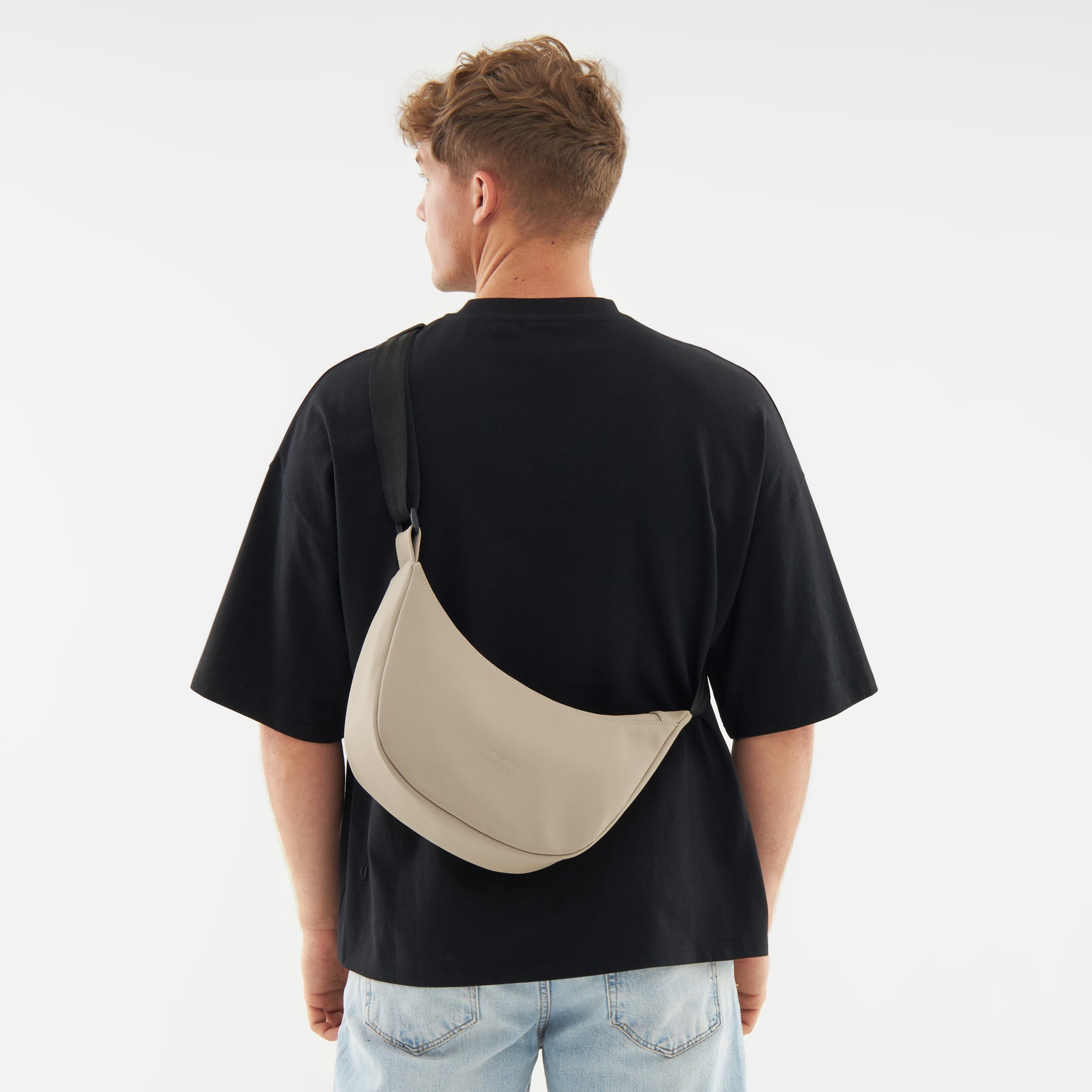 Beiger Half Moon Bag 'Rory' von Johnny Urban, getragen über der Schulter eines Mannes mit schwarzem T-Shirt und blauer Jeans