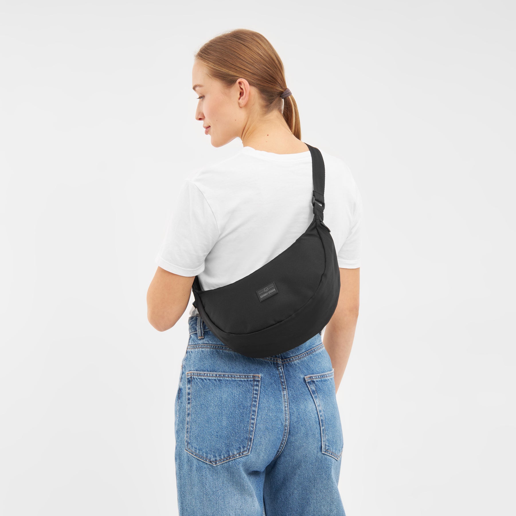 Frau von hinten mit schwarzer Half Moon Umhängetasche 'Ally Medium', weißem T-Shirt und blauen Jeans