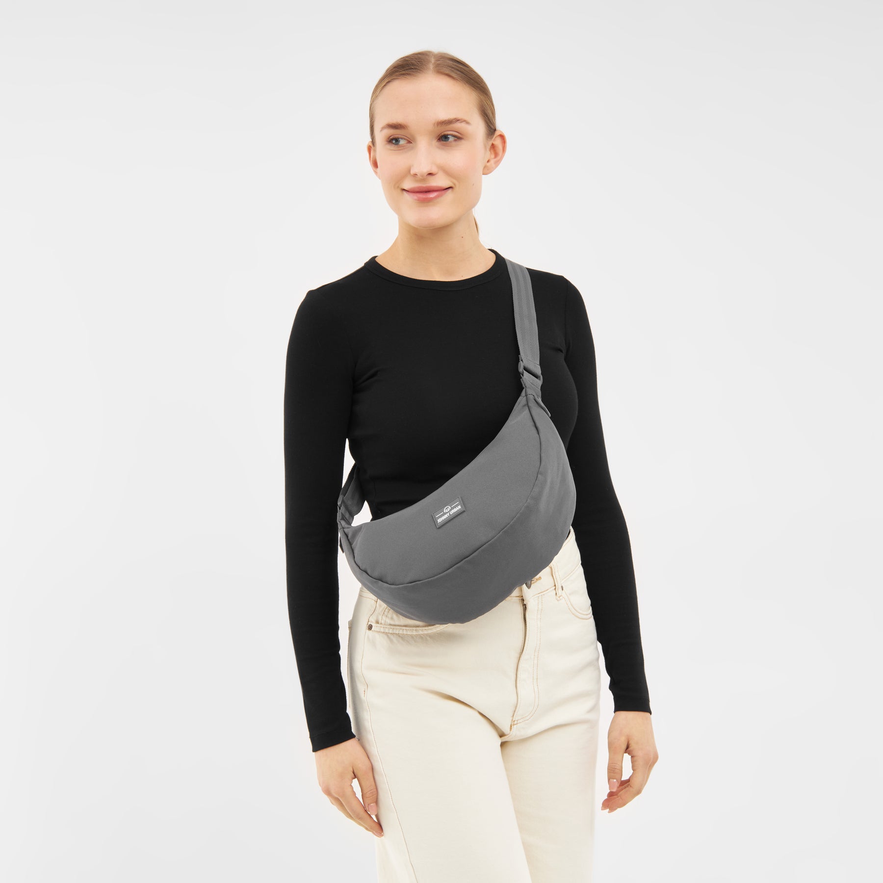 Frau mit schwarzem Langarmshirt und hellen Hosen trägt halbrunde, graue Half Moon Bag 'Ally Medium' quer über dem Oberkörper