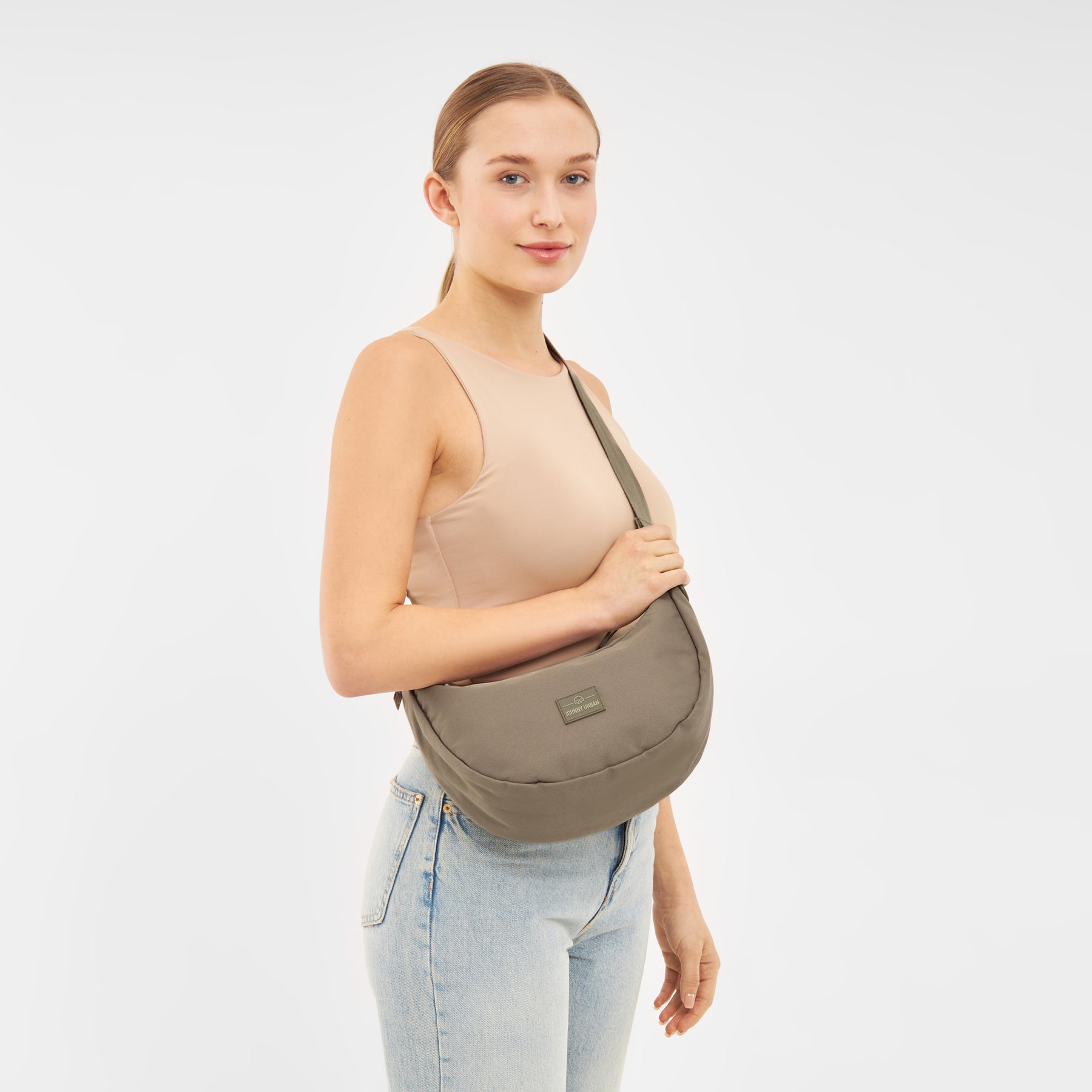 Frau trägt halbrunde Umhängetasche 'Ally Medium' in taupefarben kombiniert mit beige Top und blauen Jeans