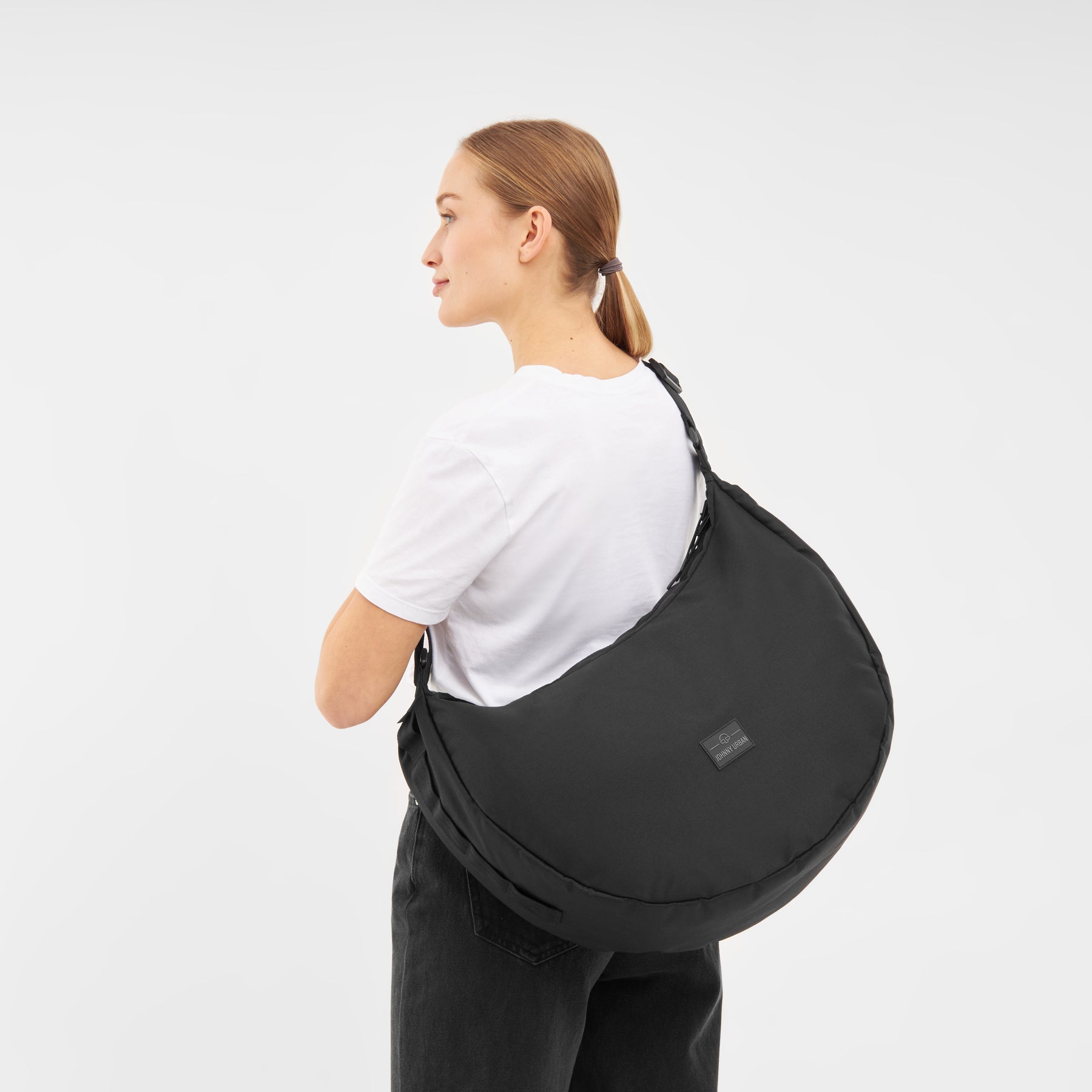 Frau trägt schwarze Half Moon Bag 'Ally XL' Schultertasche von Johnny Urban über weißem T-Shirt und schwarzer Hose