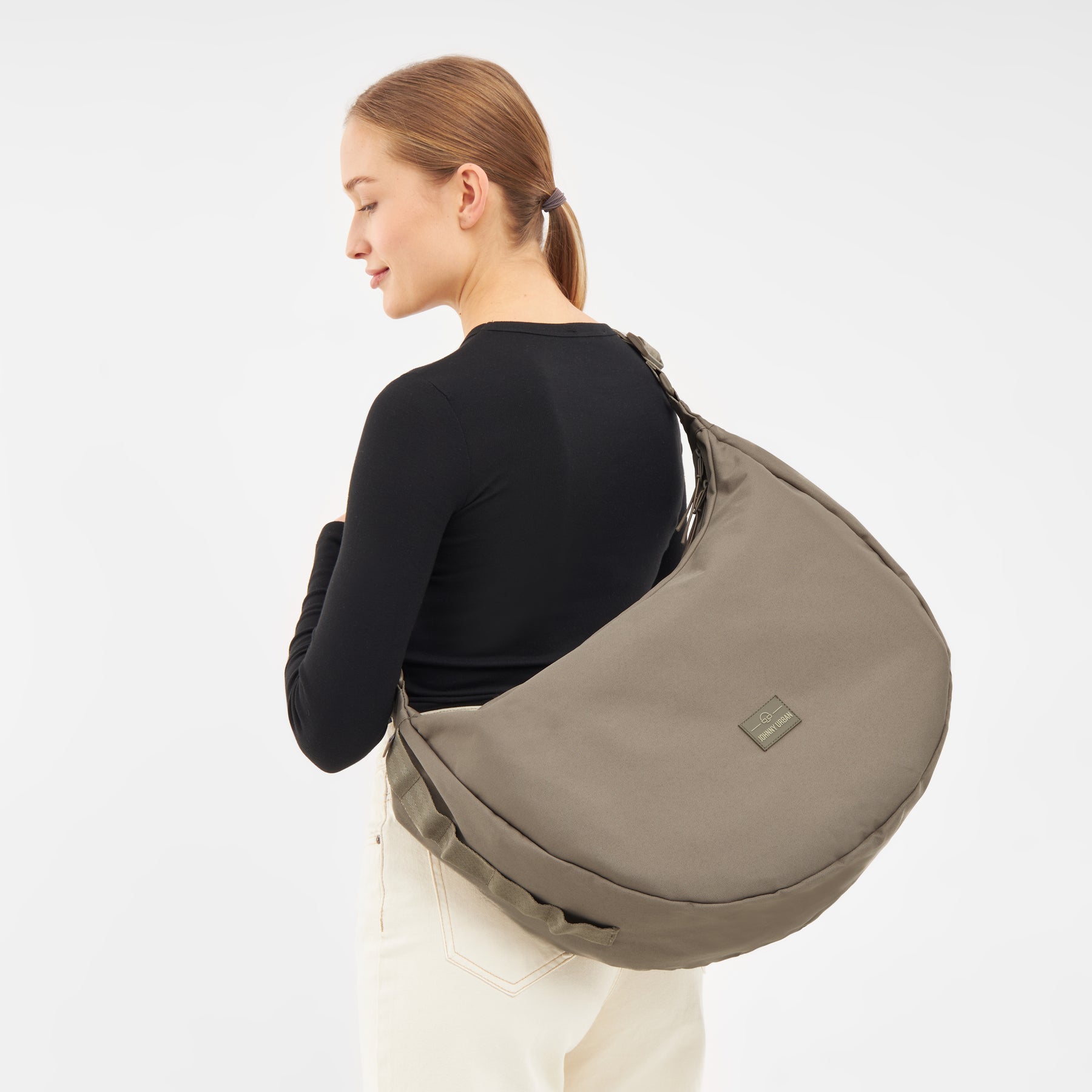 Frau mit schwarzem Oberteil trägt die halbmondförmige Half Moon Bag 'Ally XL' in graubraun über der Schulter