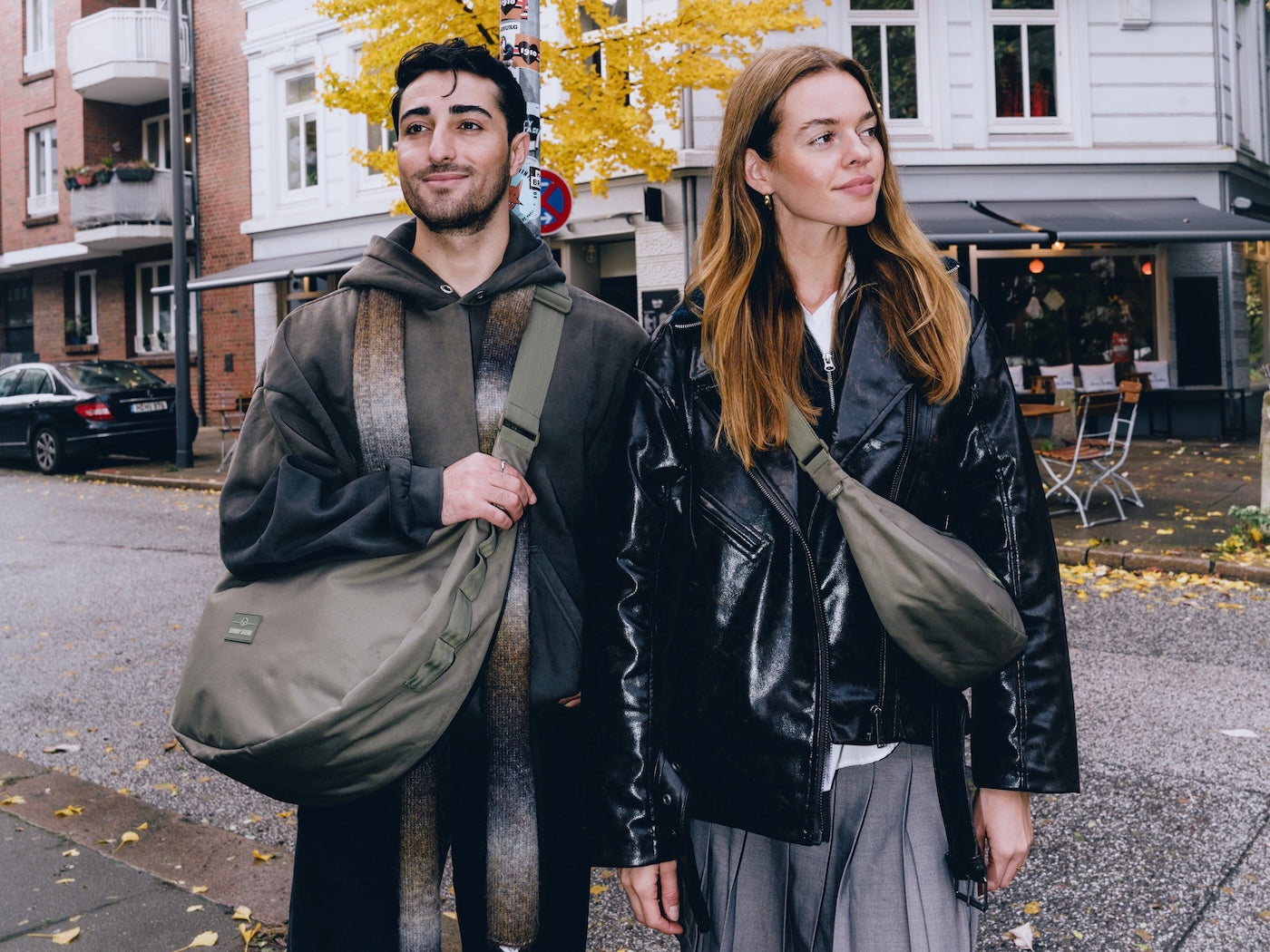 Mann mit großem olivgrünem Half Moon Bag und Frau mit kleinerem olivgrünem Half Moon Bag Ally Medium auf Stadtstraße im Herbst