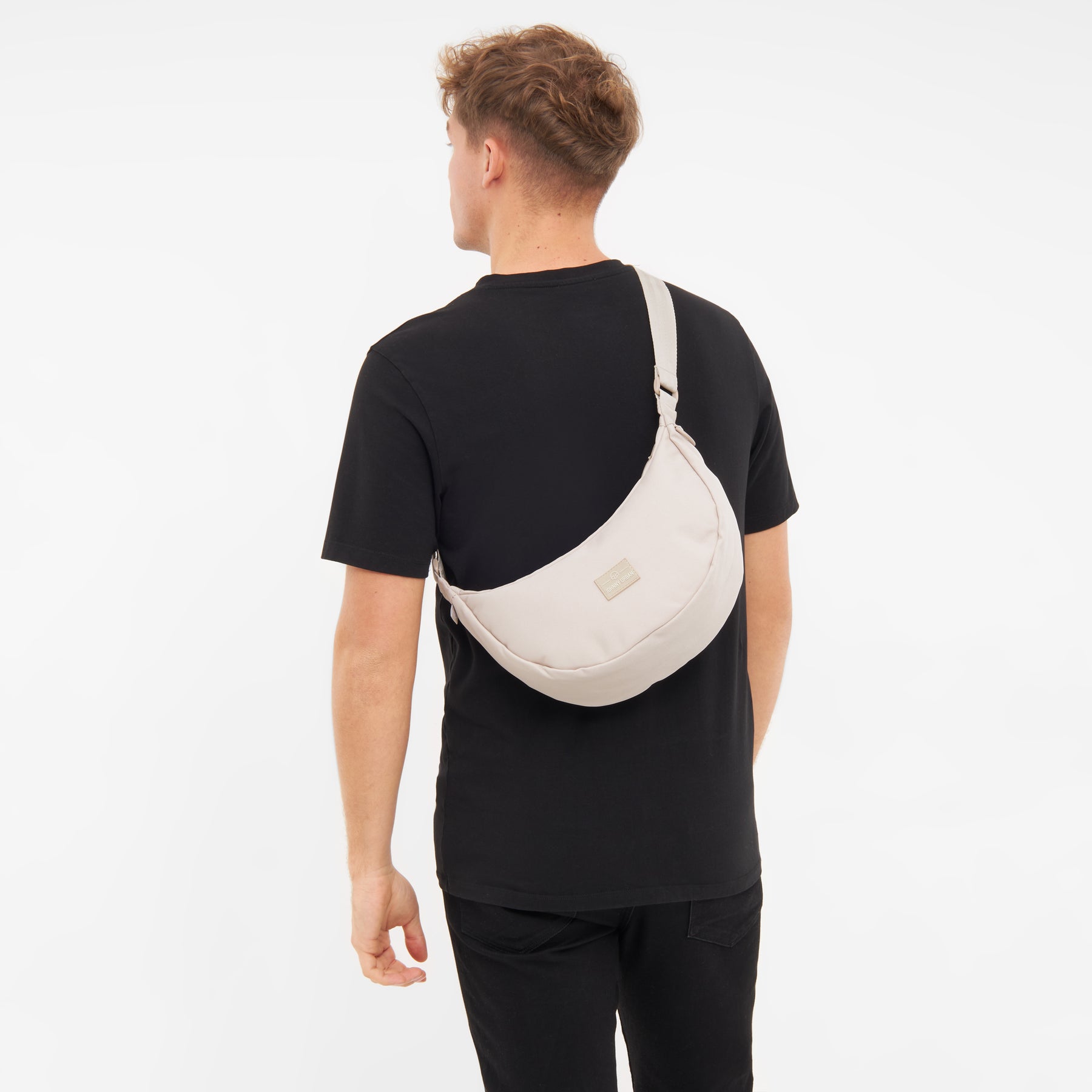 Mann mit schwarzem T-Shirt trägt die halbrunde Tasche 'Ally Medium' in hellem Farbton über der Schulter