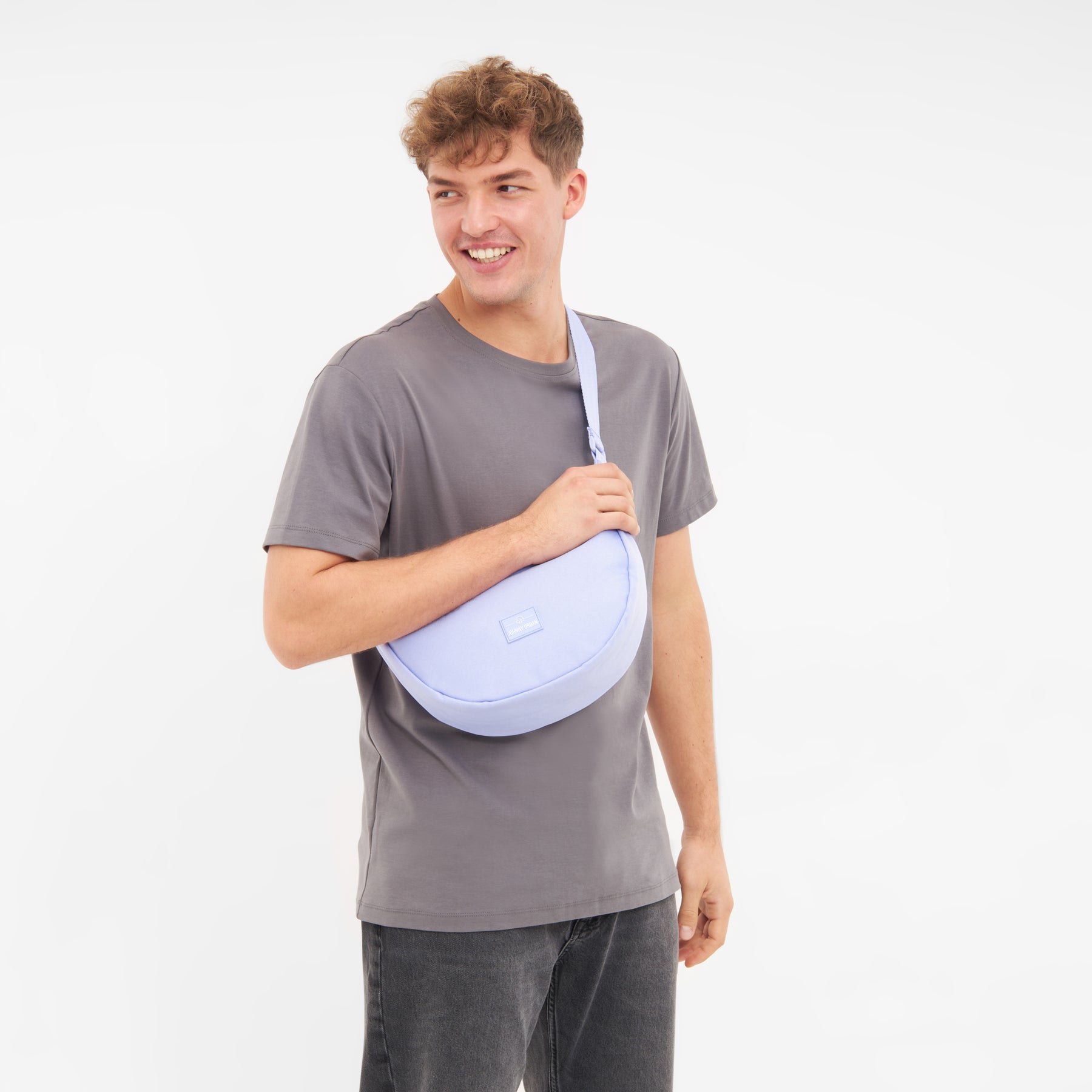 Mann trägt die lilafarbene Half Moon Bag 'Ally Medium' über der Schulter mit grauem T-Shirt und dunkler Hose