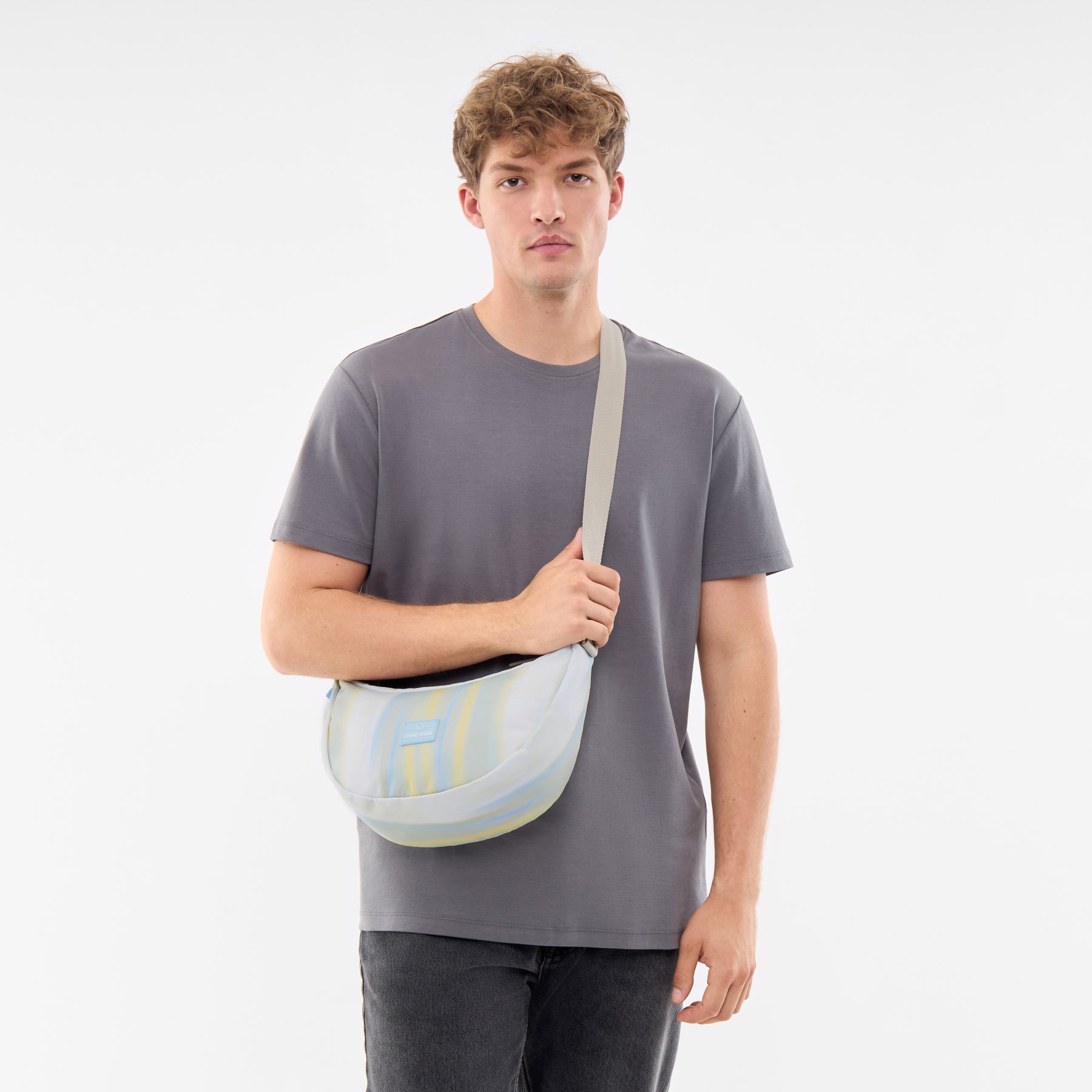 Mann trägt Half Moon Bag 'Ally Medium' quer über der Schulter, farblich gestreift in Pastelltönen