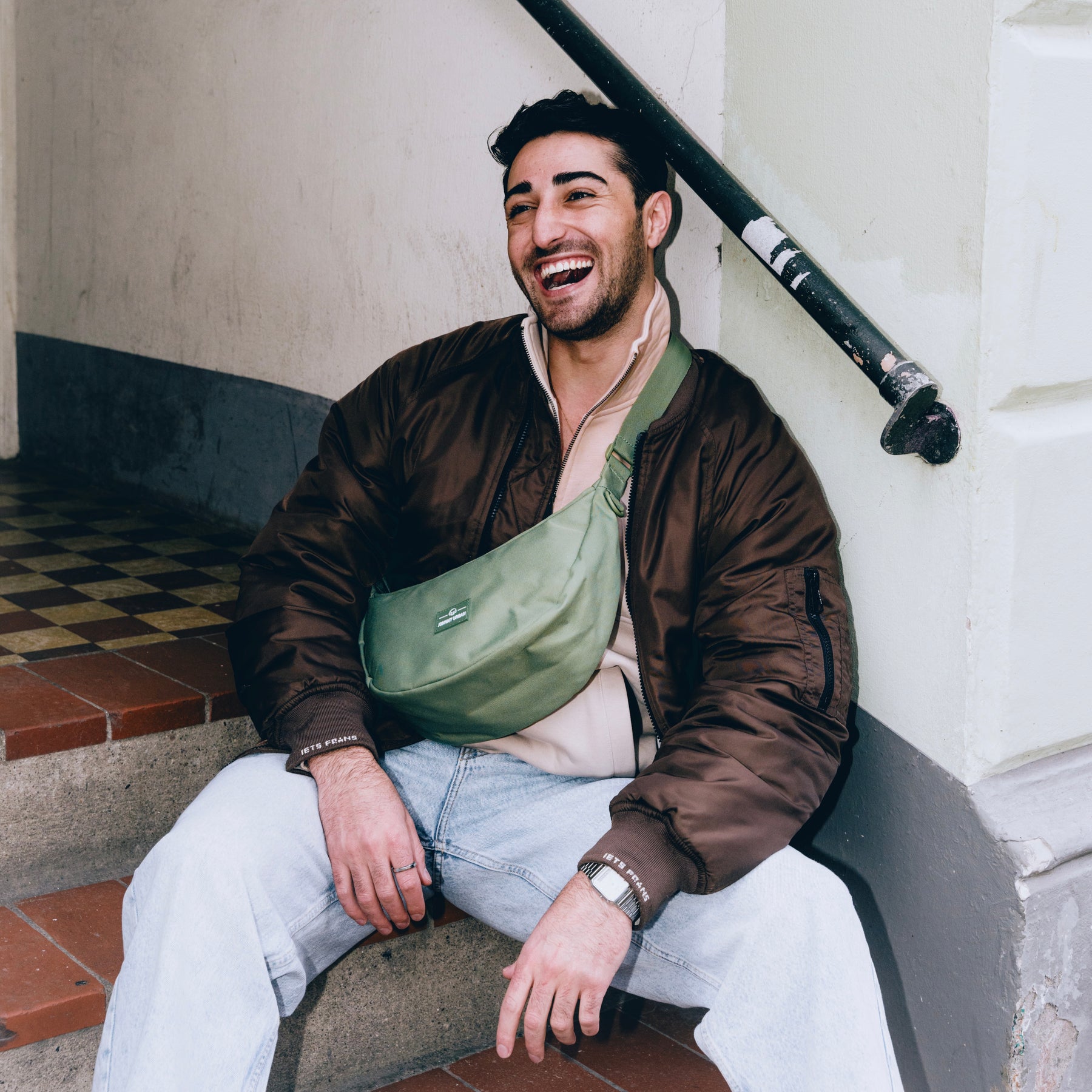 Mann sitzt auf Treppe mit grüner Half Moon Bag 'Ally Medium' quer über der Brust