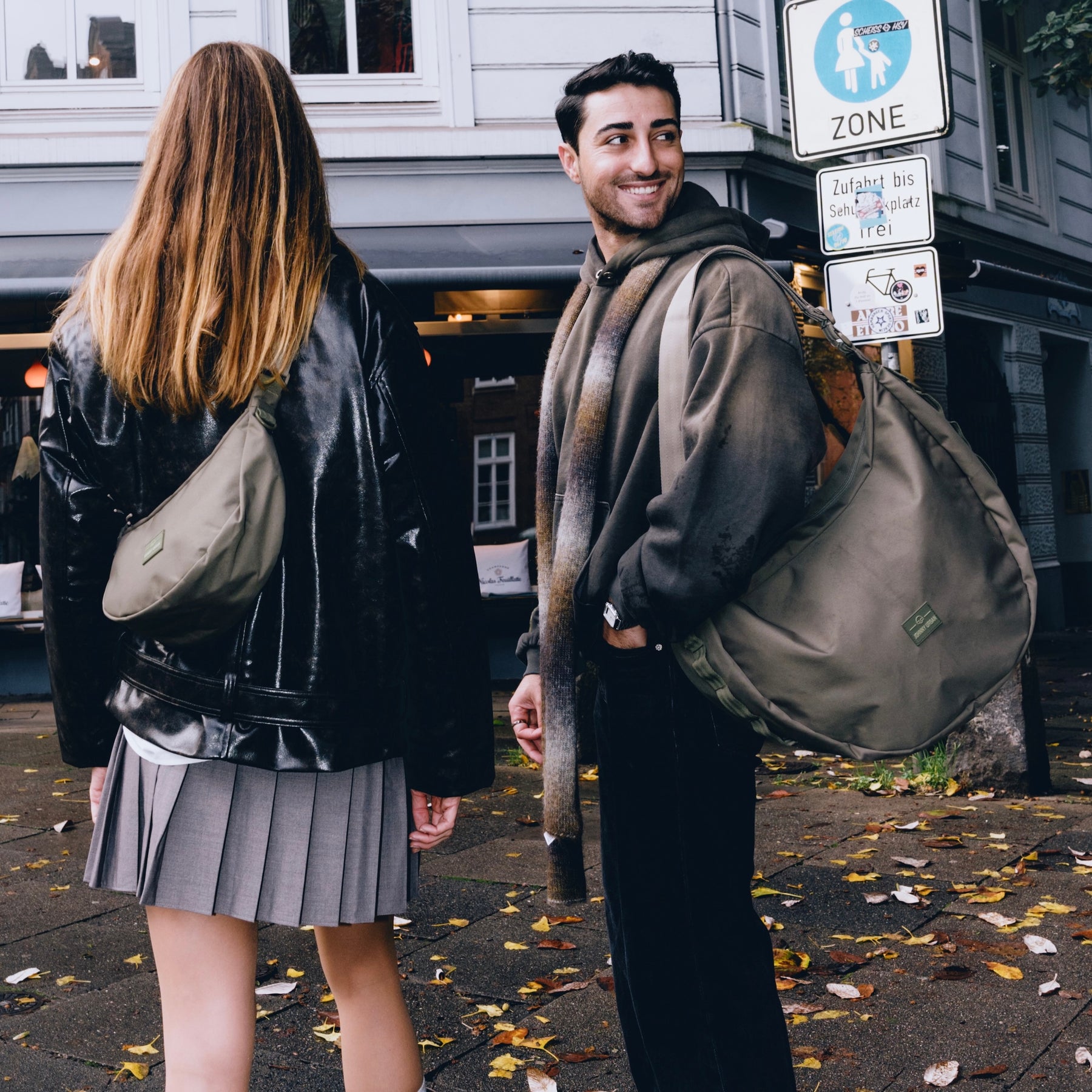 Mann und Frau tragen halbmondförmige Johnny Urban 'Ally XL' Taschen in Olivegrün in einer städtischen Umgebung