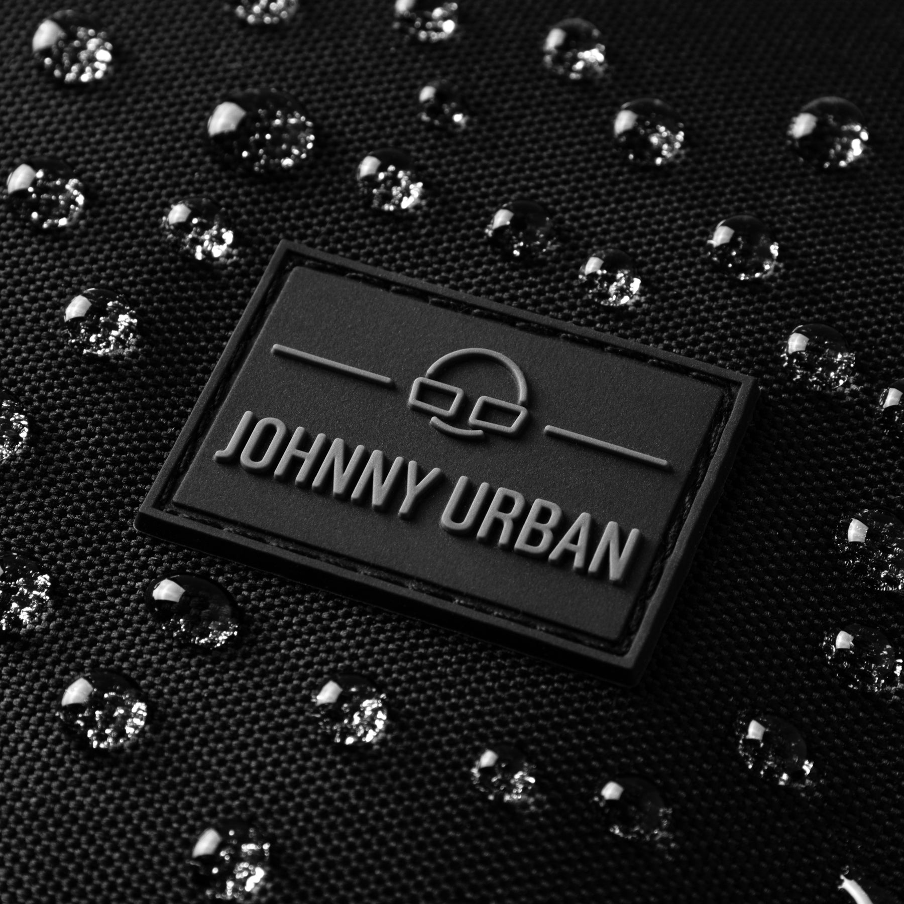 Wasserabweisendes schwarzes Material mit Johnny Urban Logo und Wassertropfen
