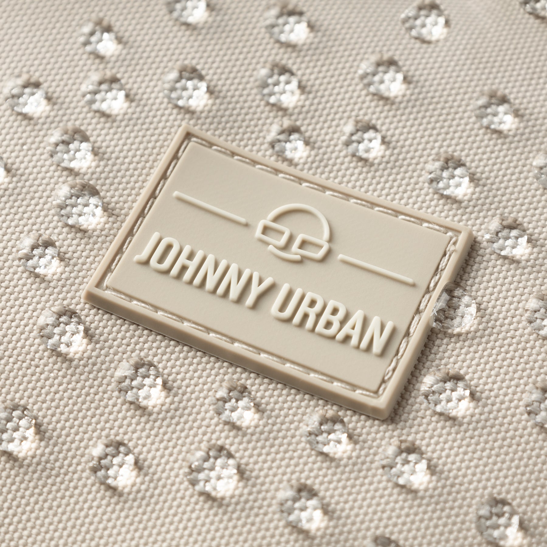 Nahaufnahme des Johnny Urban Logos auf wasserabweisendem hellbeigem Stoff mit Wassertropfen