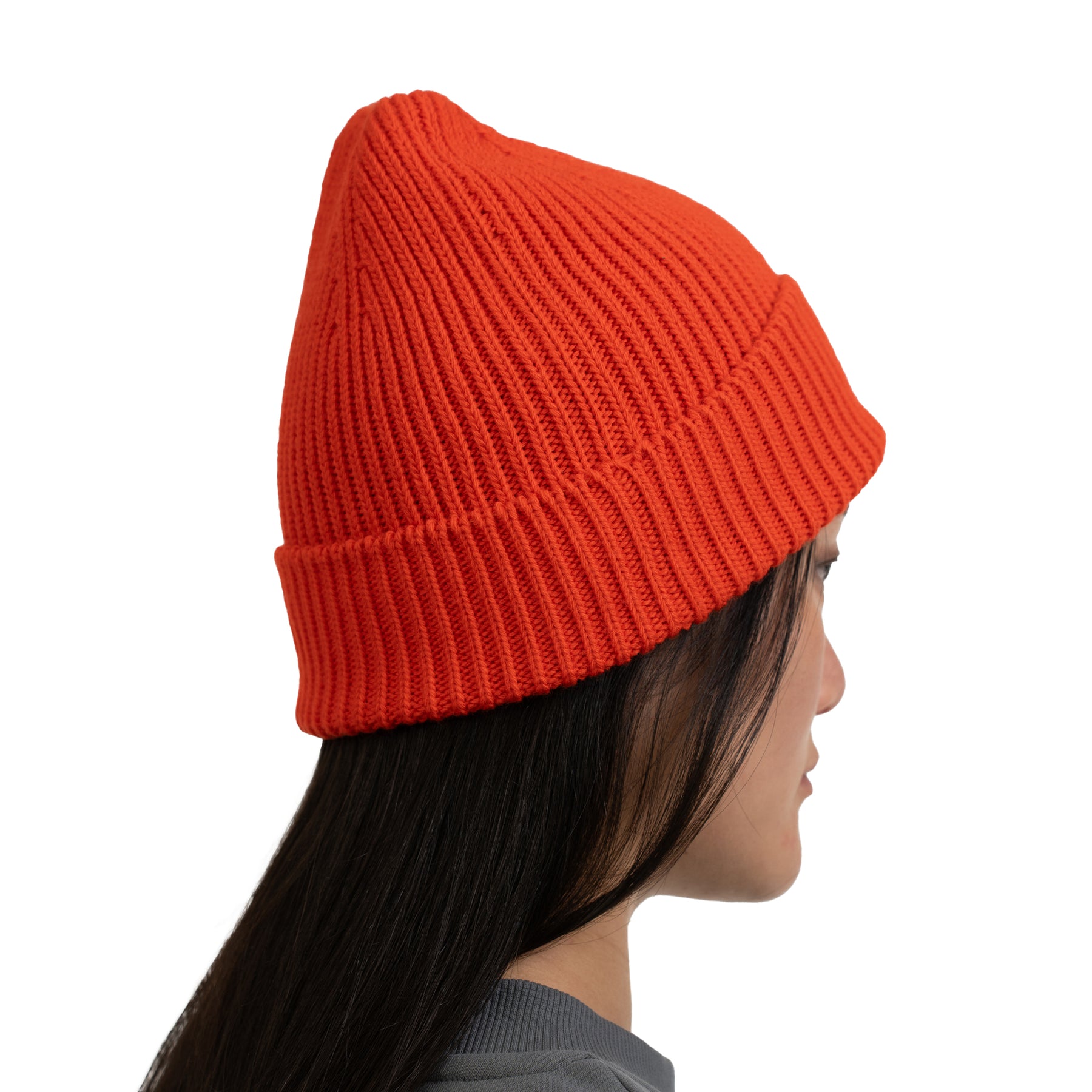 Seitliches Profil einer Frau mit langem dunklem Haar, die die orange-rote Mütze 'Billie' trägt