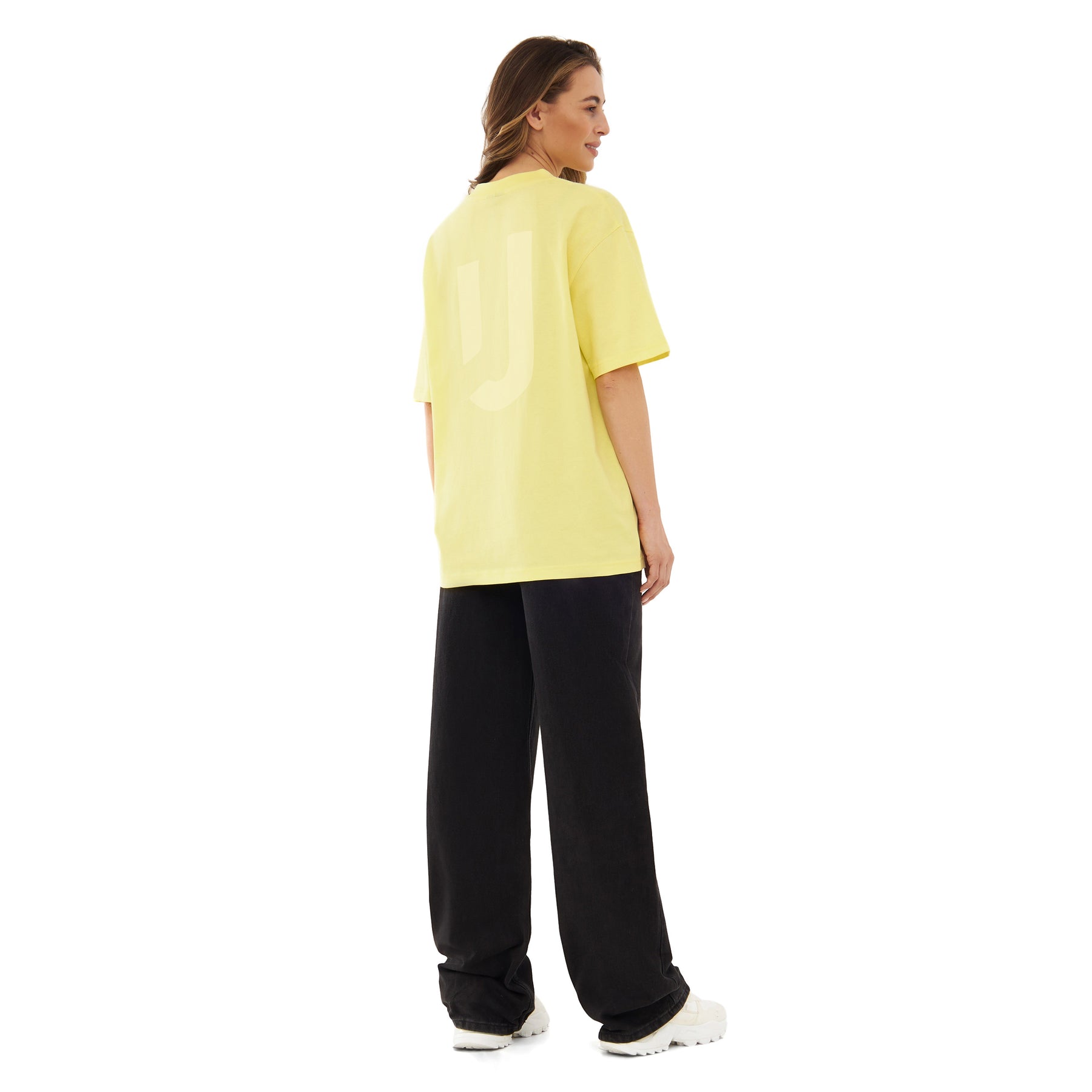 Frau trägt oversized gelbes T-Shirt 'Sammy JU' von Johnny Urban, schwarze Hose, weiße Schuhe, Rückenansicht