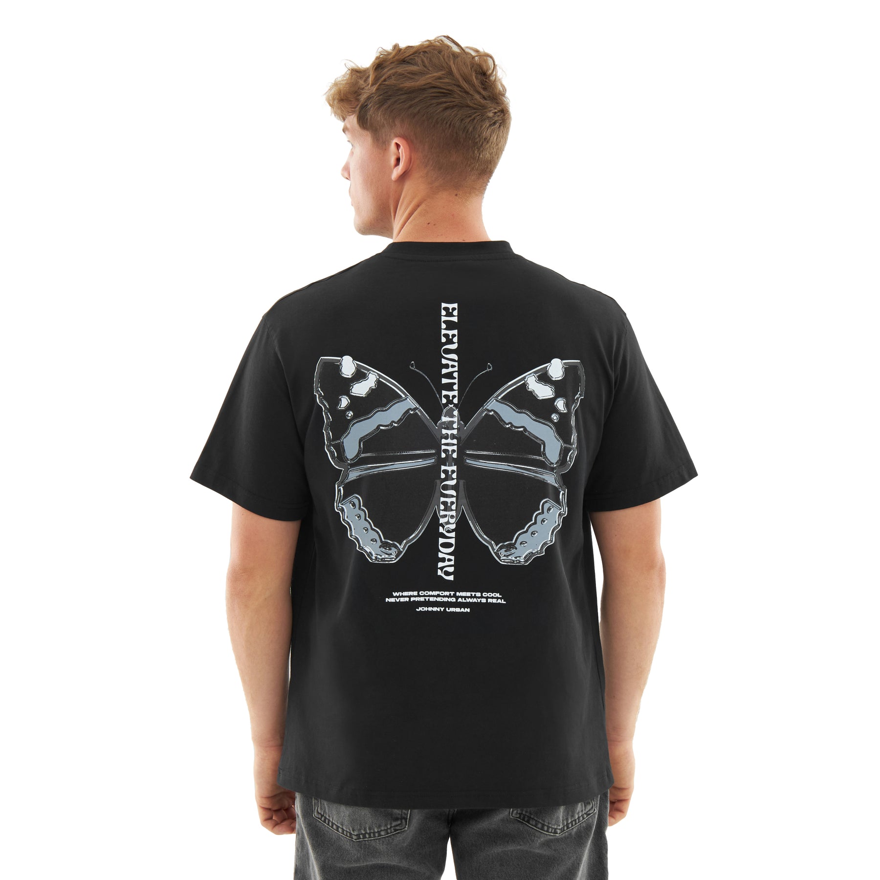 Mann trägt schwarzen Oversize-T-Shirt 'Sammy Chrome Butterfly' mit grauem Schmetterlingsprint und senkrechtem Schriftzug 'ELEVATE THE EVERY DAY' auf dem Rücken