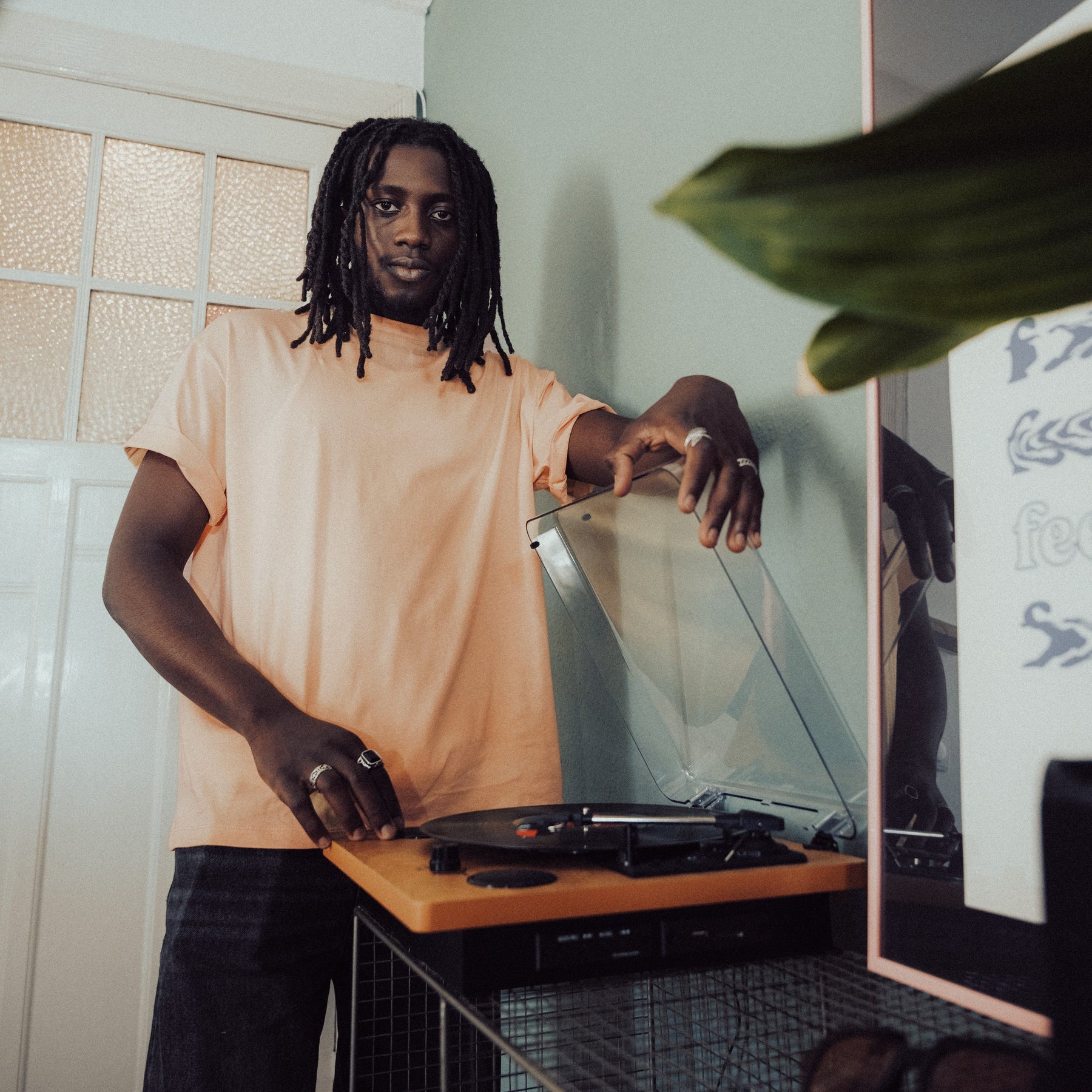 Mann mit Dreadlocks in peachfarbenem Oversize-T-Shirt 'Sammy' von Johnny Urban neben Plattenspieler