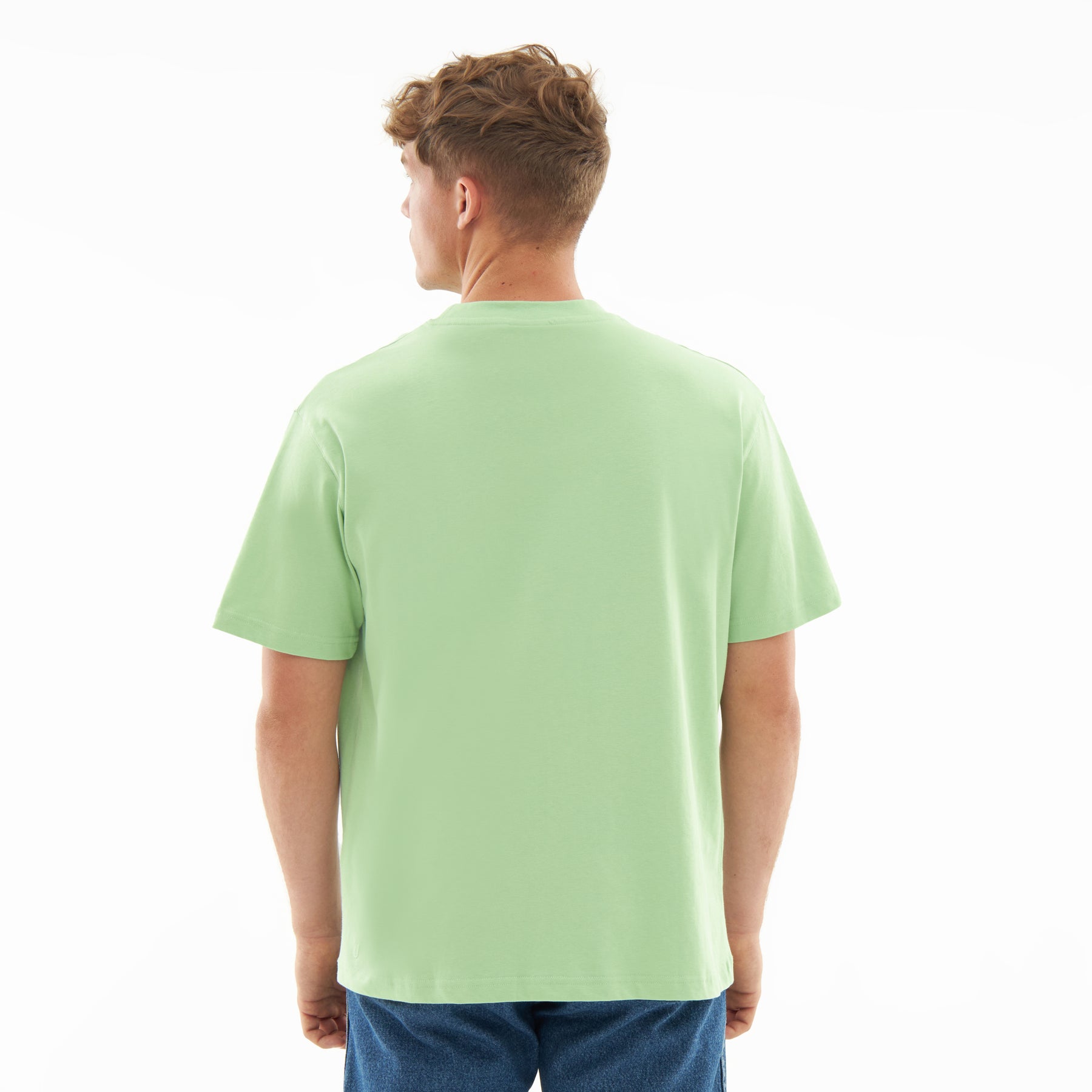 Mann trägt oversized T-Shirt 'Sammy' in Salbeigrün, Rückansicht, kombiniert mit blauer Jeans