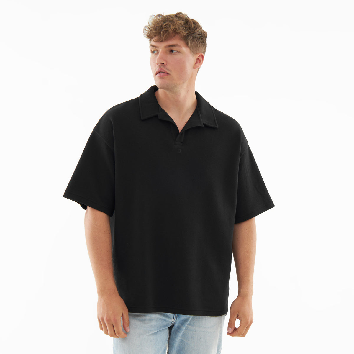 Mann trägt schwarzes Poloshirt mit kurzem Arm und offenem Kragen, dazu helle Jeans