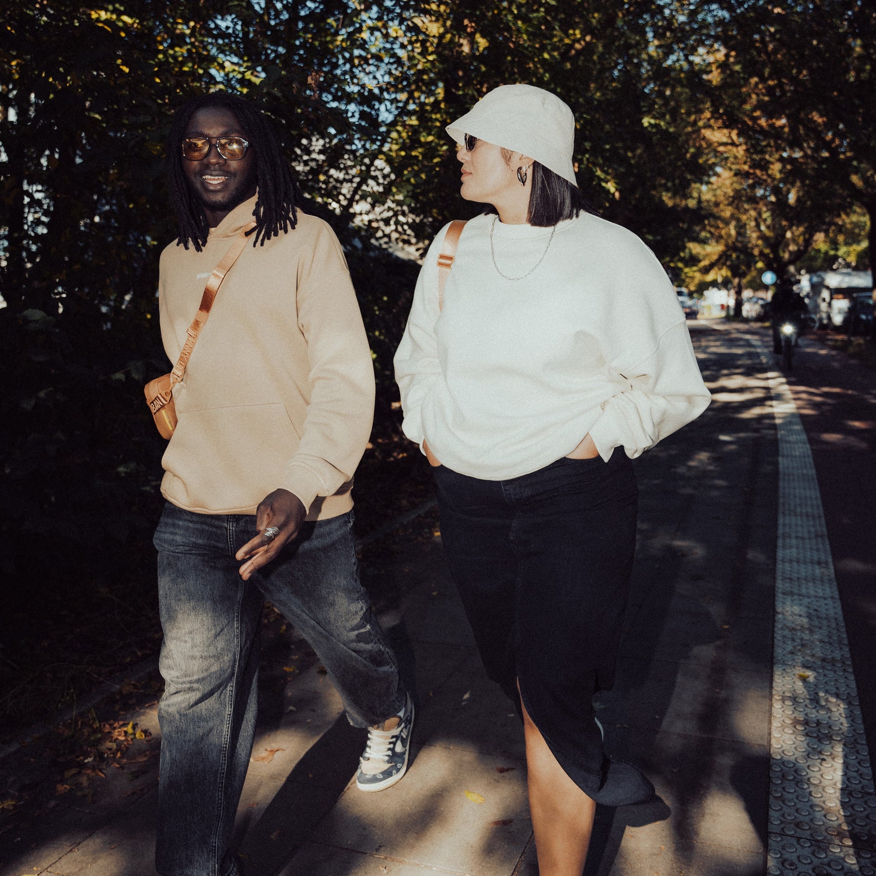 Zwei Menschen gehen draußen, eine trägt weißen oversized Crewneck 'Carter' Pullover, schwarze Jeans und Hut