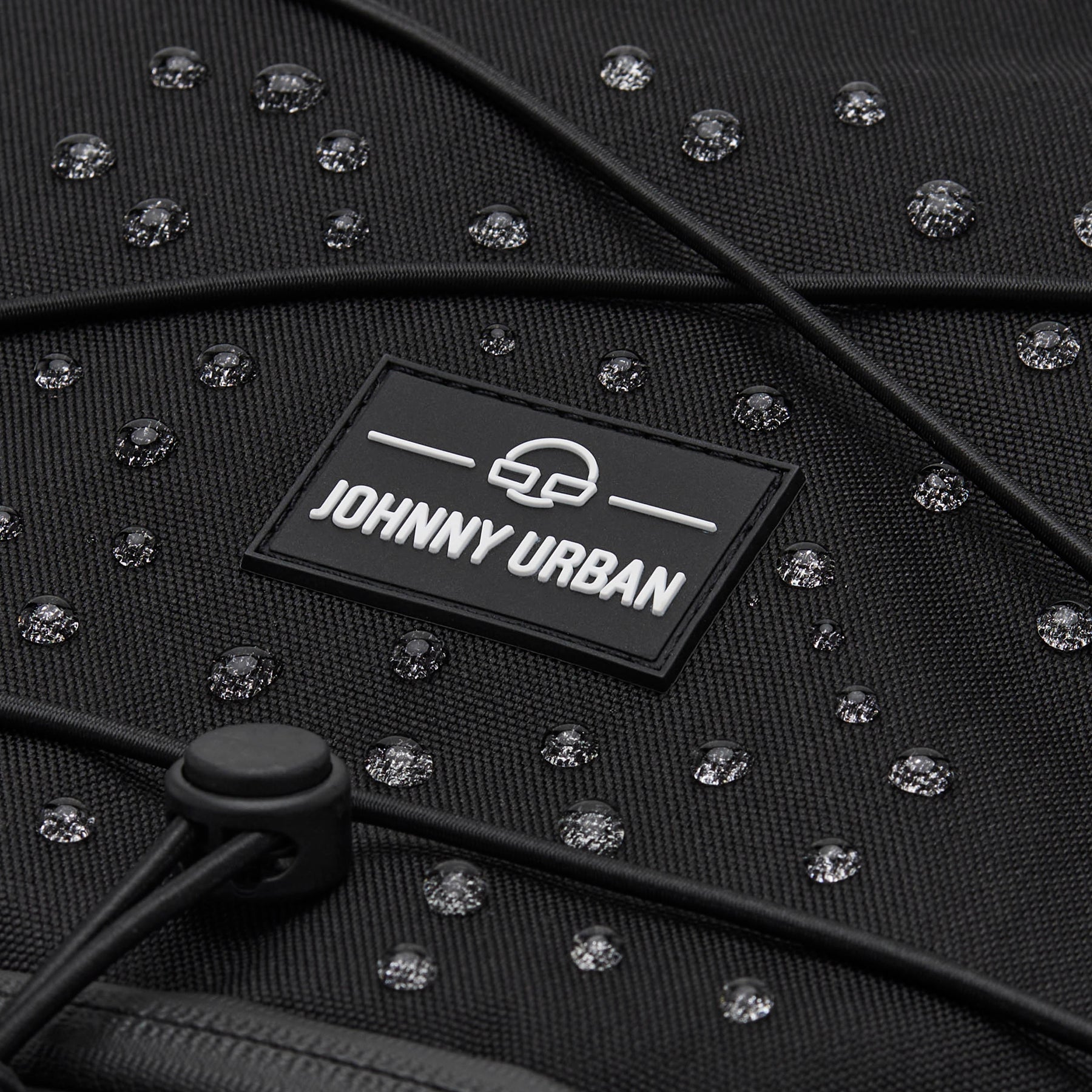 Nahe Aufnahme des schwarzen, wasserabweisenden Reiserucksacks Allen Large Travel von Johnny Urban mit sichtbaren Wassertropfen