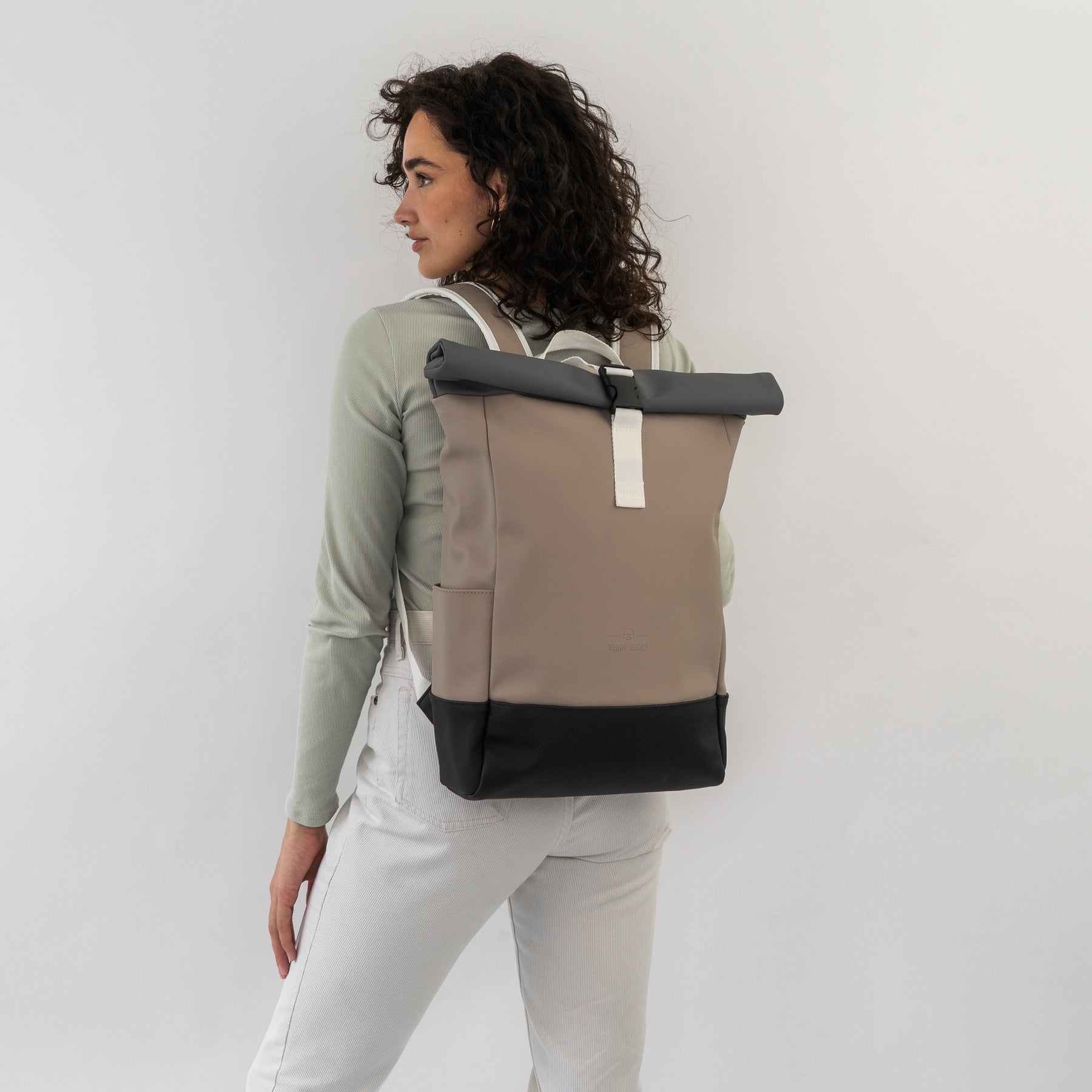 Frau mit Rolltop-Rucksack 'Harvey Medium' in Beige, Grau und Schwarz, trägt ihn an den weißen Hosen und grünem Oberteil rückseitig