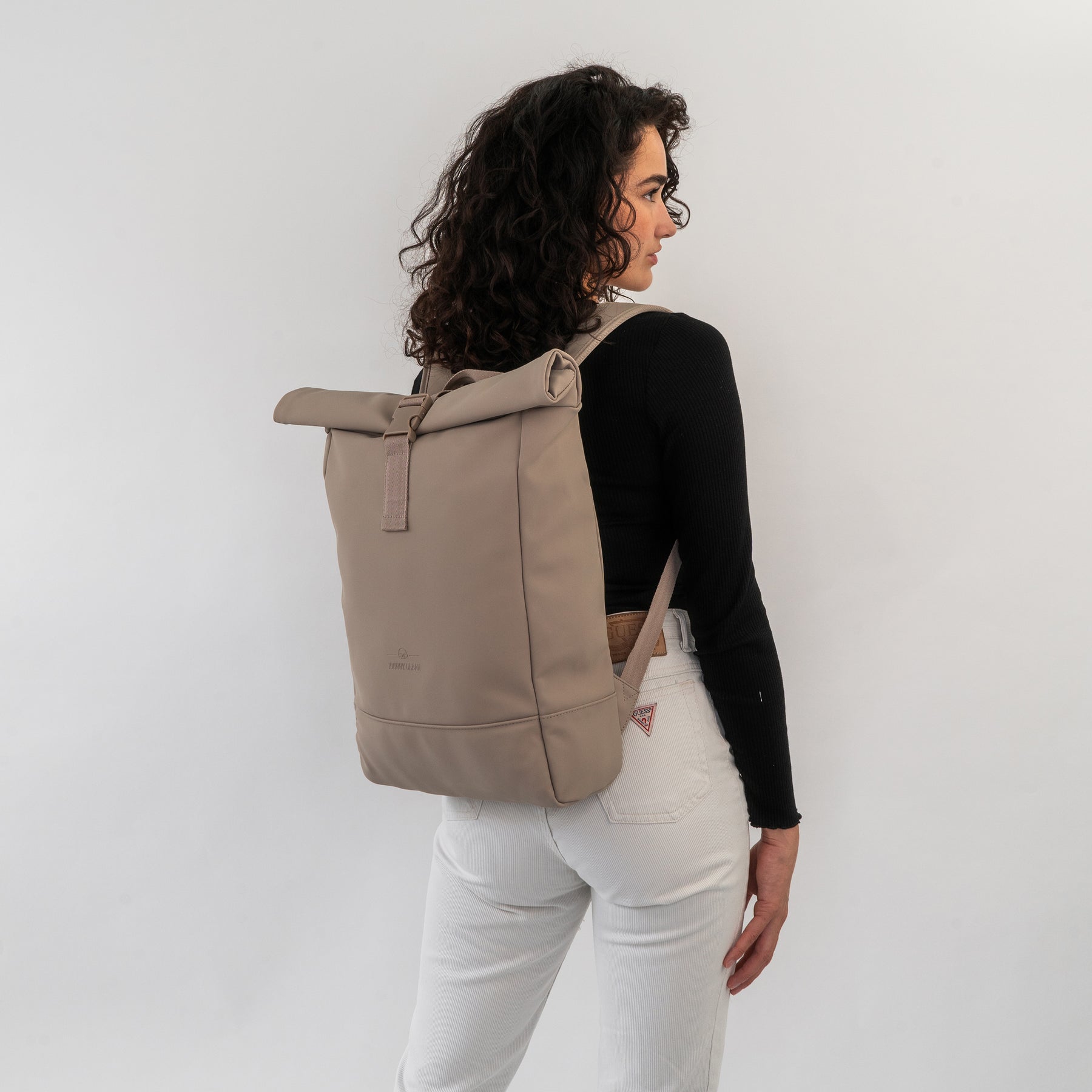 Frau mit lockigen Haaren trägt den beigen Rolltop Rucksack 'Harvey Medium' von Johnny Urban