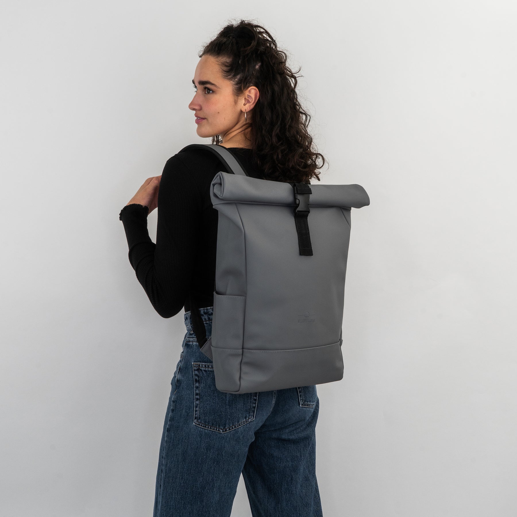 Frau trägt grauen Rolltop Rucksack 'Harvey Medium' mit schwarzem Verschluss und Trägern