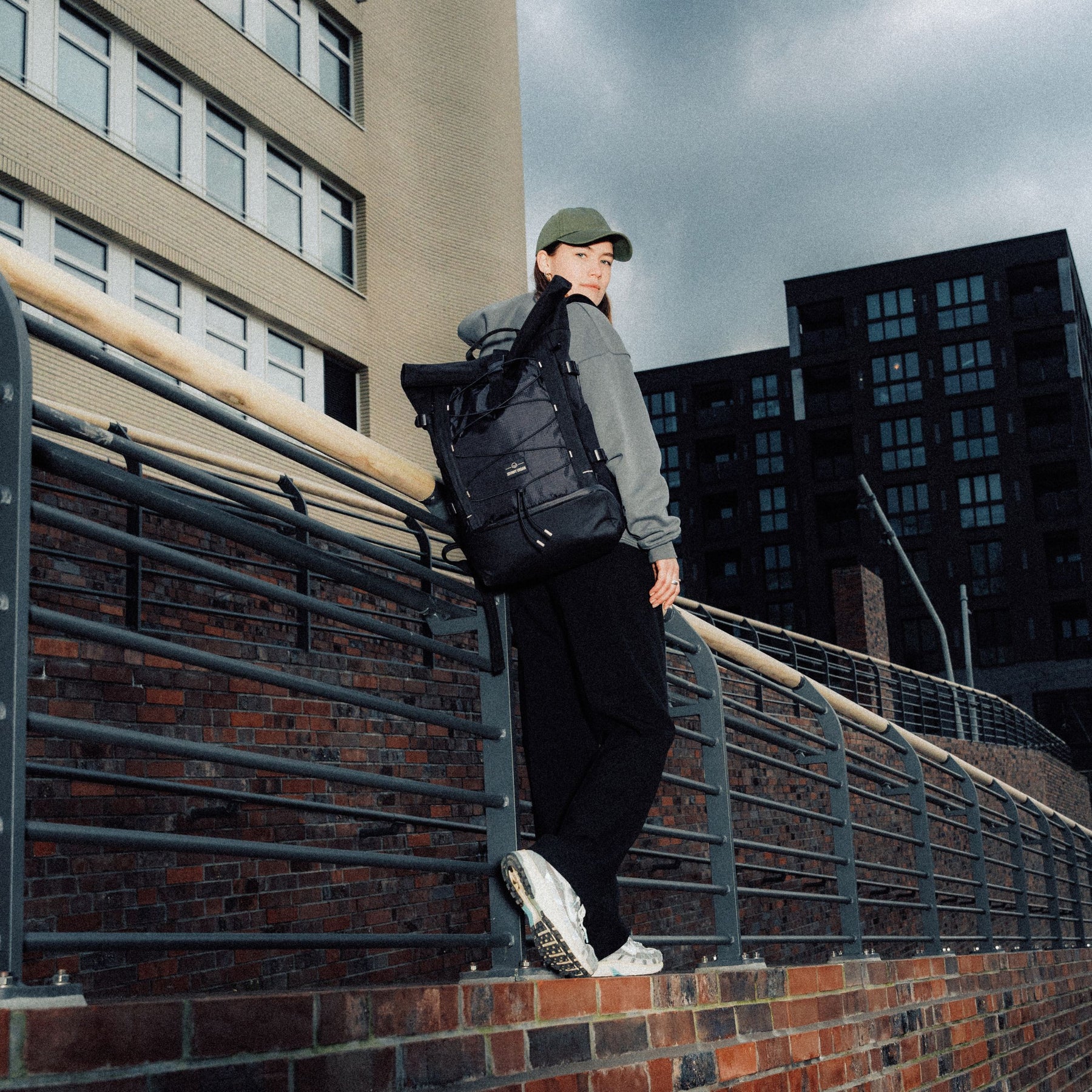 Frau mit grünem Cap trägt schwarzen Rolltop Rucksack 'Allen Large Move' urban vor Gebäuden